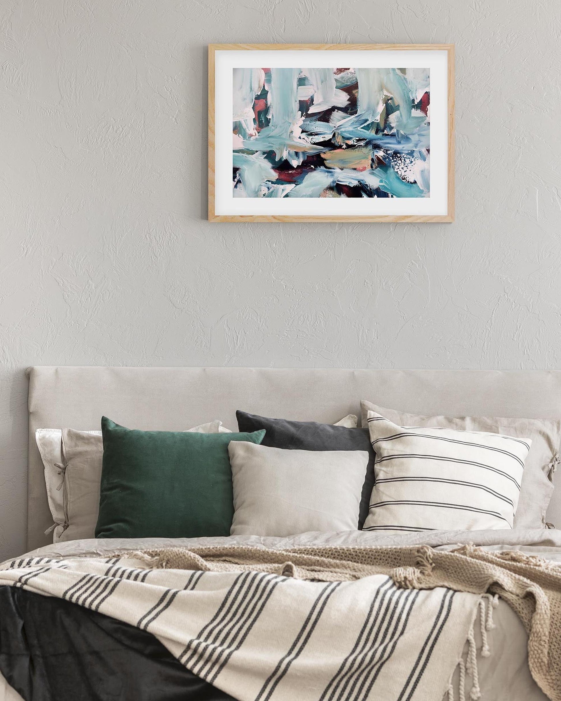 Framed abstract art above a bed with pillows and a blanket.