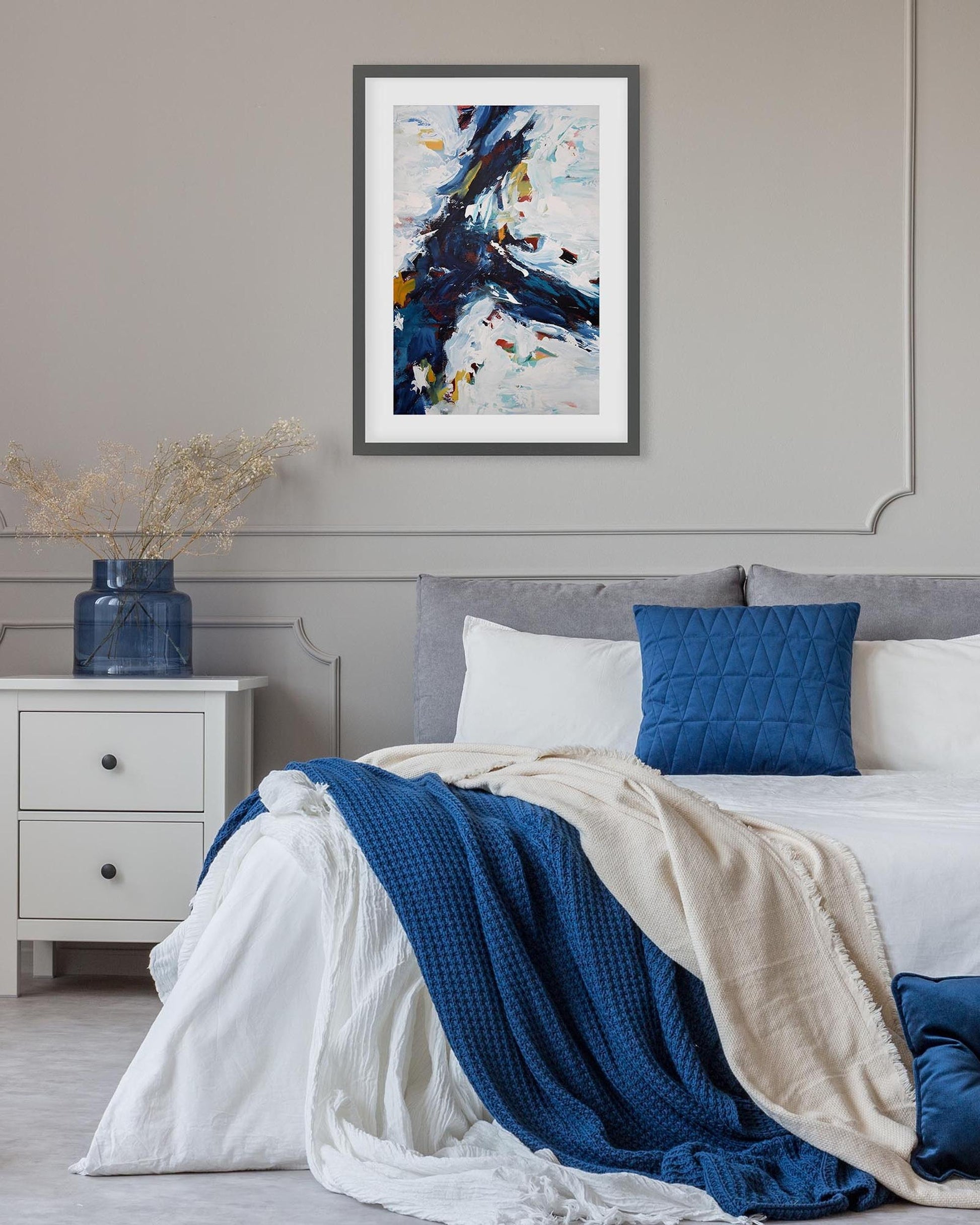 Bedroom with abstract art on the wall, nightstand, and bed with blue and white bedding.