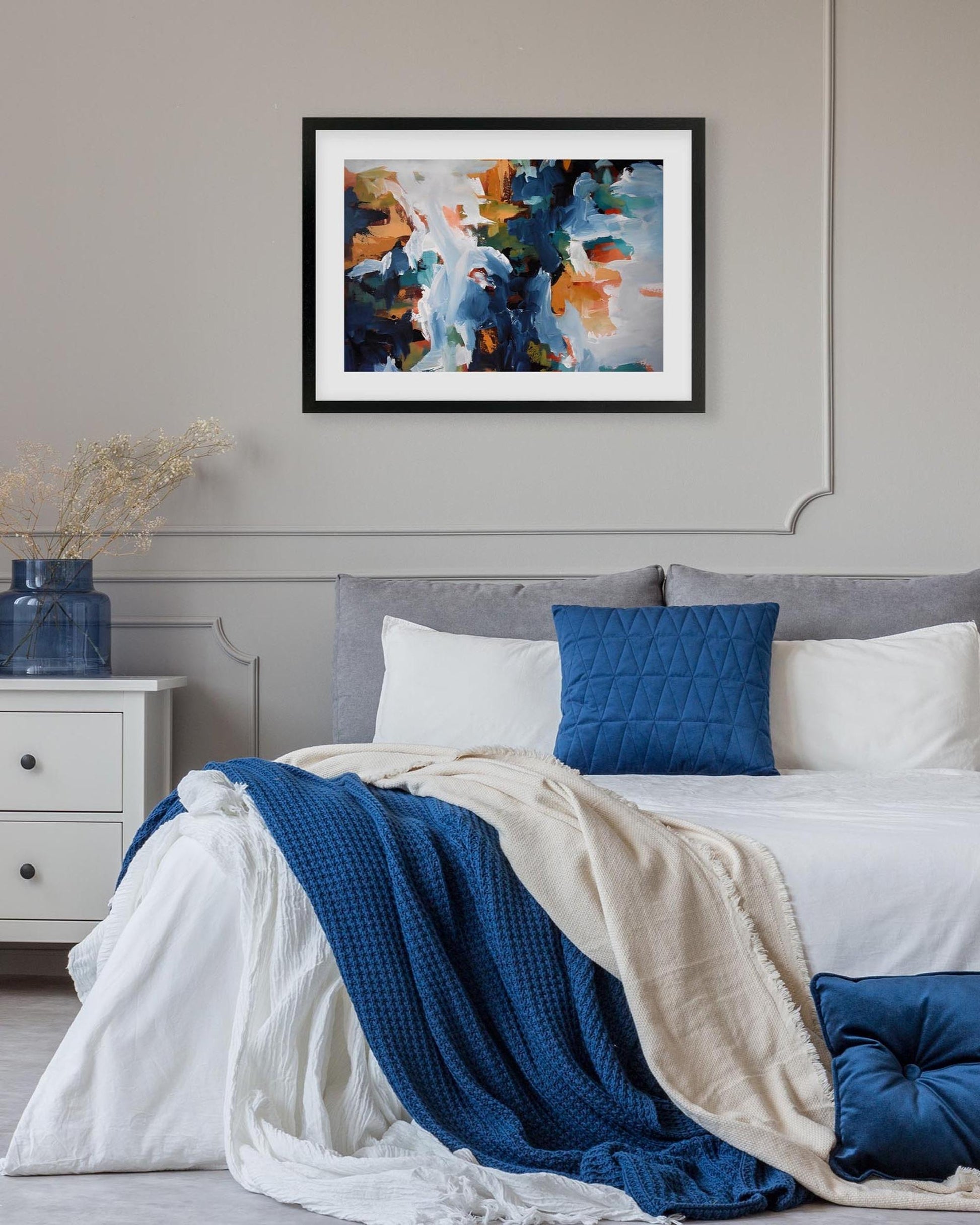 Bedroom with abstract art on the wall, bed with blue and beige bedding, and nightstand.