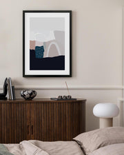 Framed abstract art piece on a wall above a wooden cabinet.