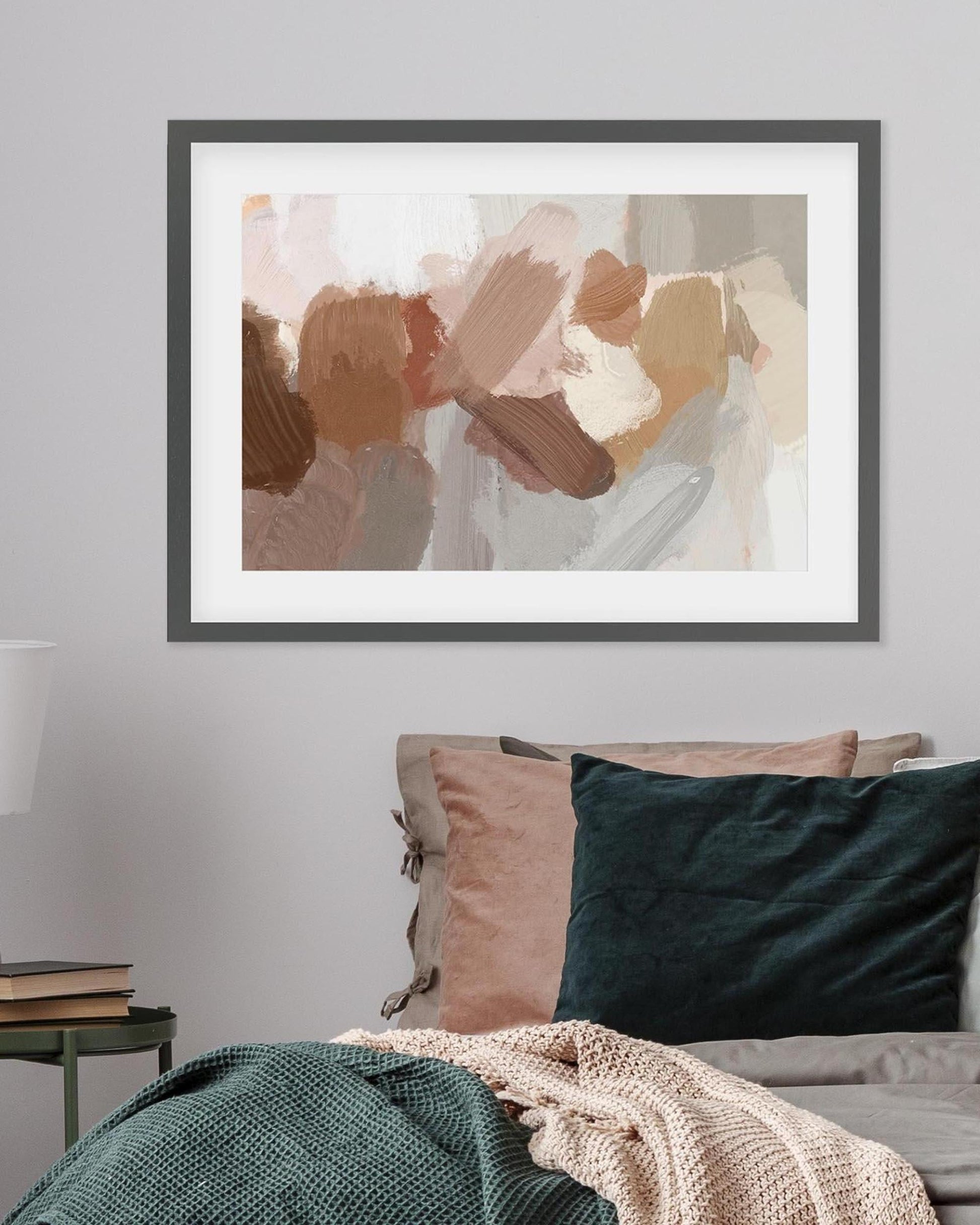 Framed abstract art piece on a wall above a bed with pillows and blankets.