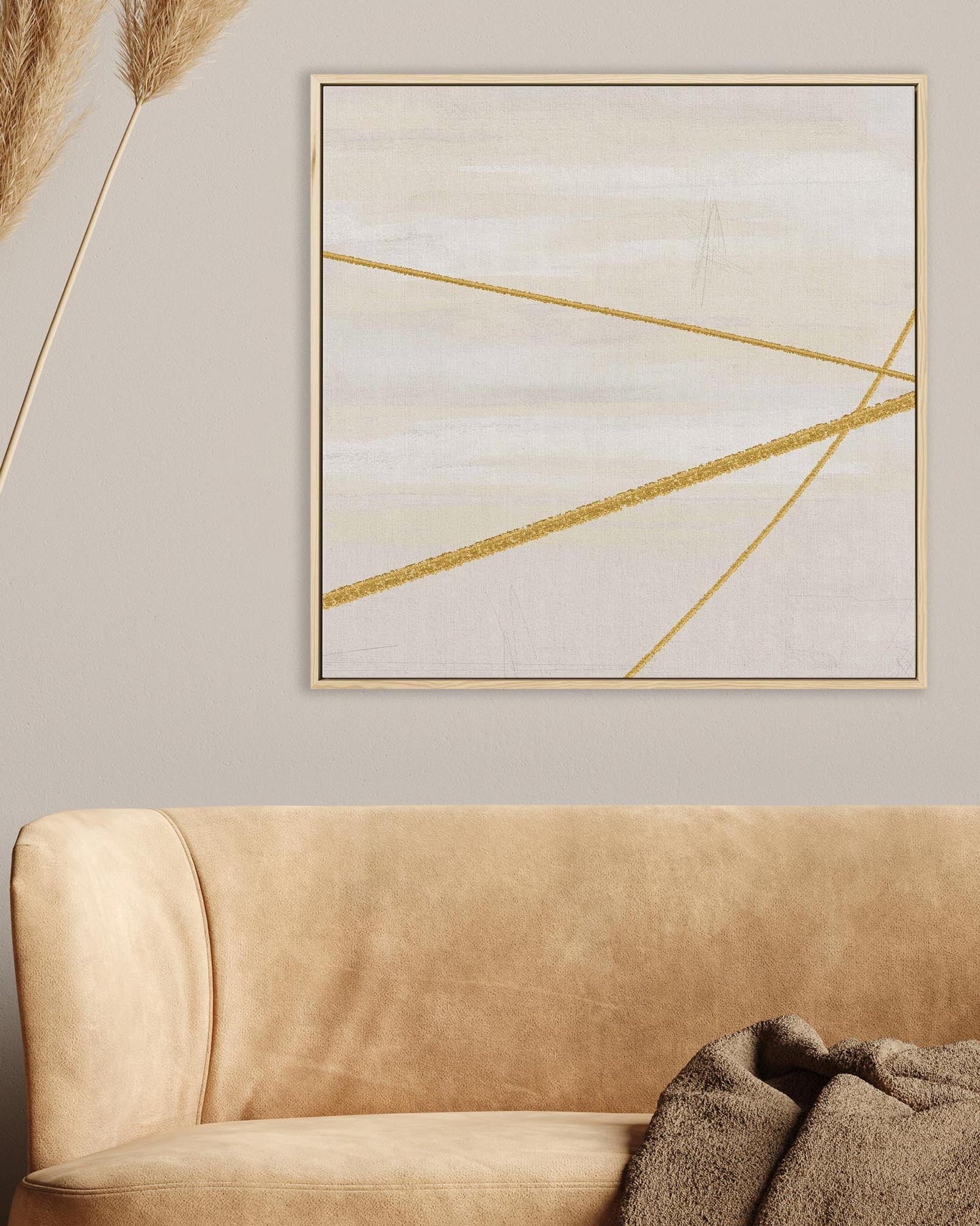 Abstract art piece with gold lines on a beige wall above a brown sofa.