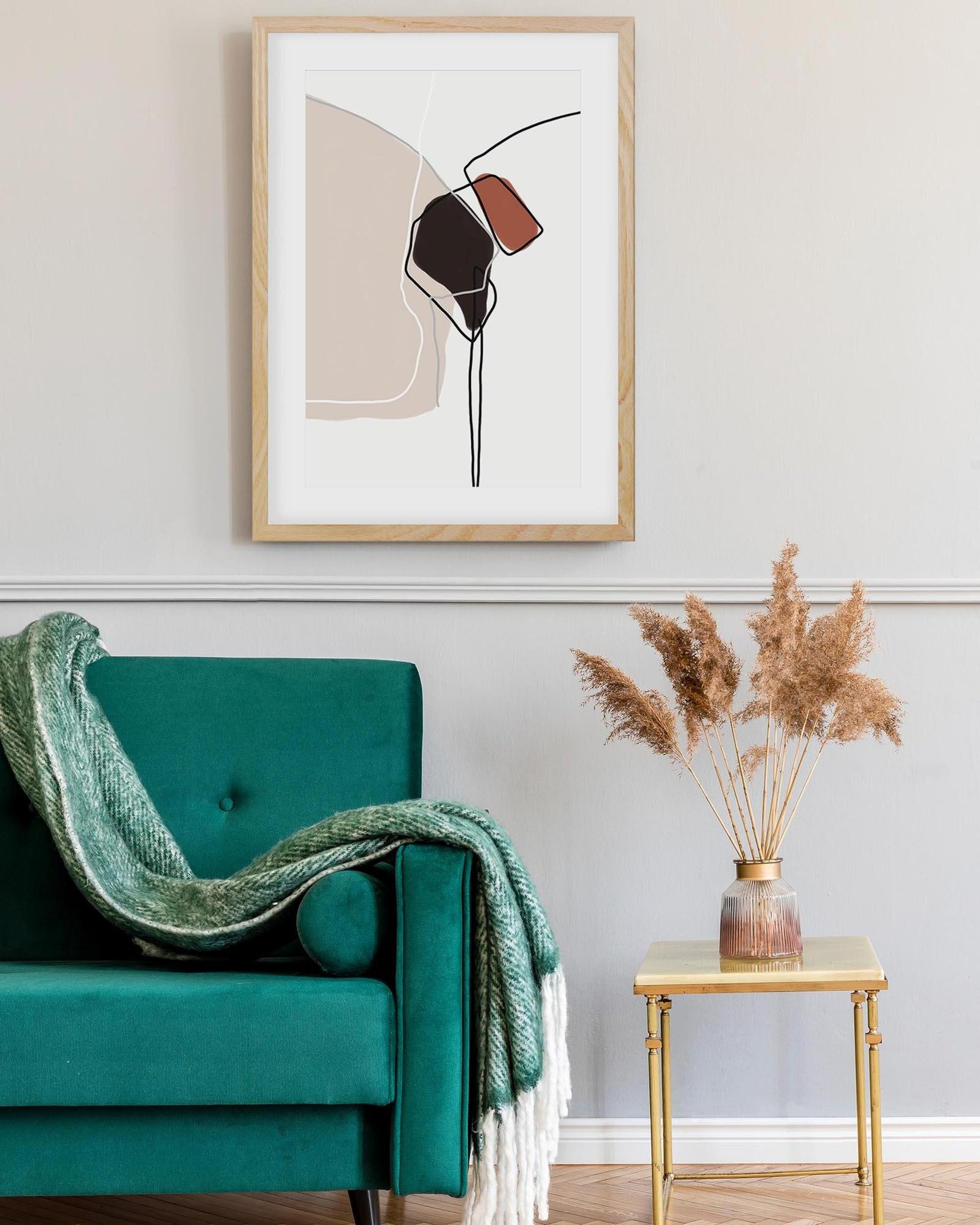 Teal armchair with a green blanket, gold side table with dried plants, and abstract art on the wall.