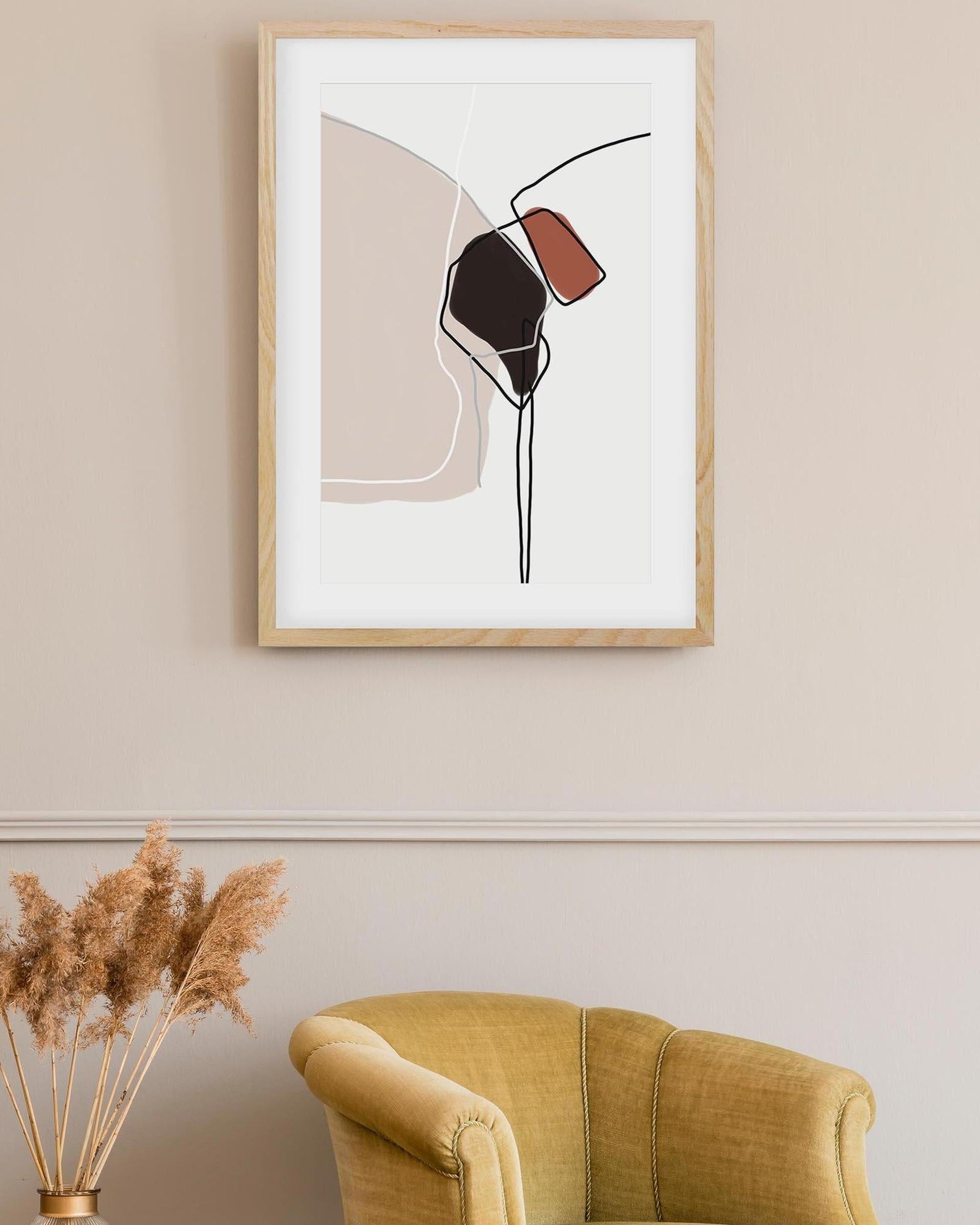 Abstract art print in a wooden frame on a beige wall above a yellow armchair.