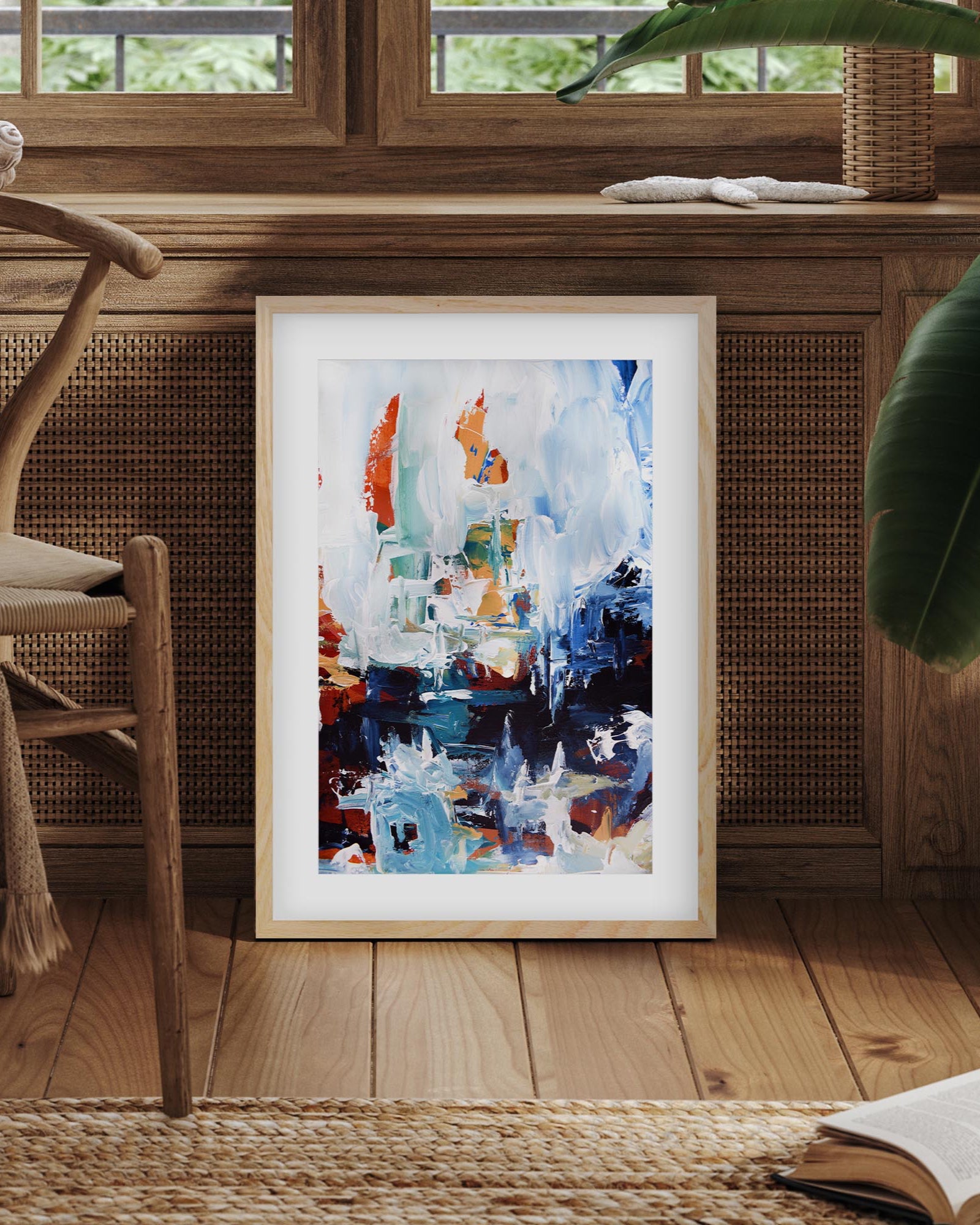 Framed abstract art piece on a wooden floor with a chair and books in the background