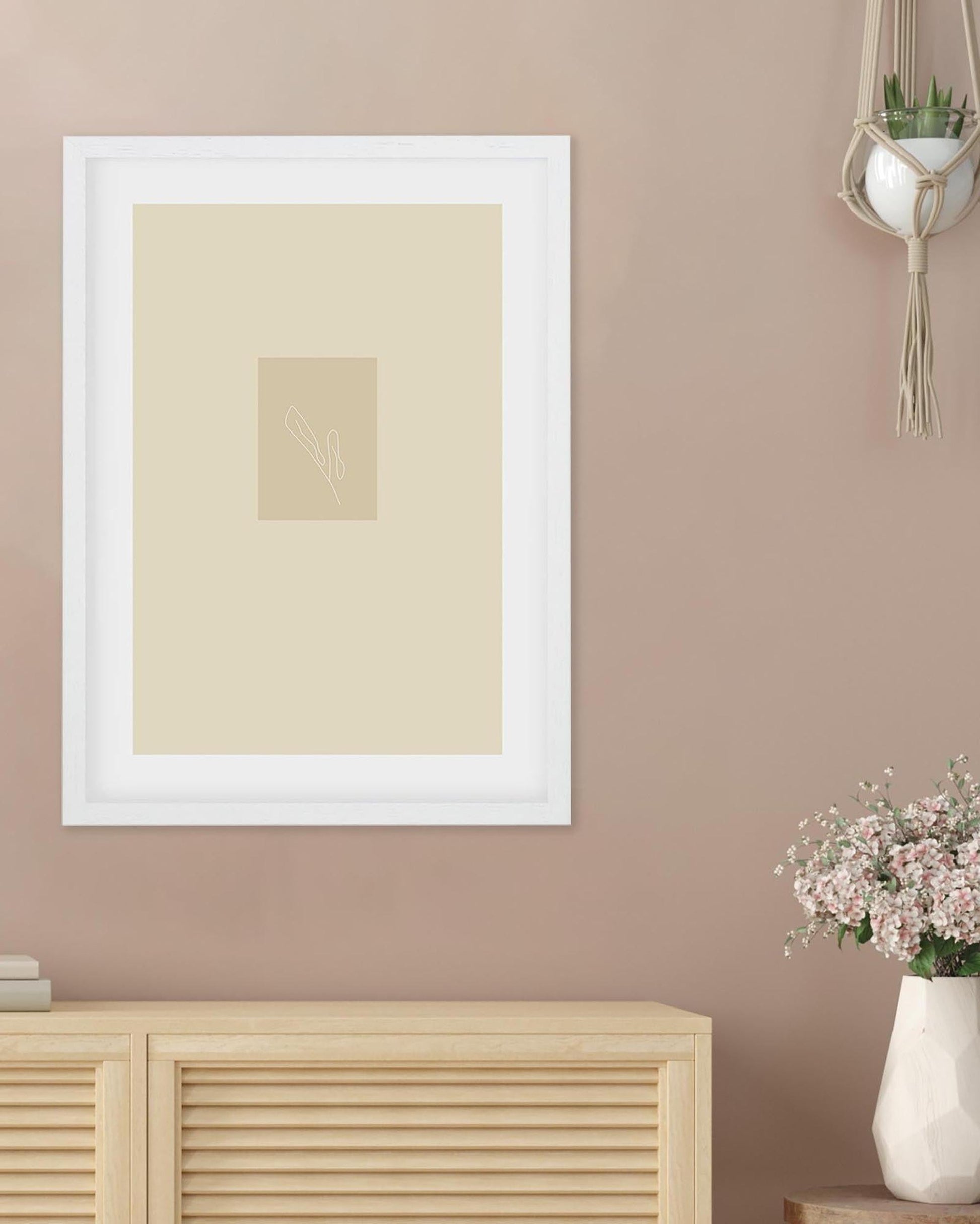 Framed beige artwork on a wall with a wooden cabinet and vase in the foreground.