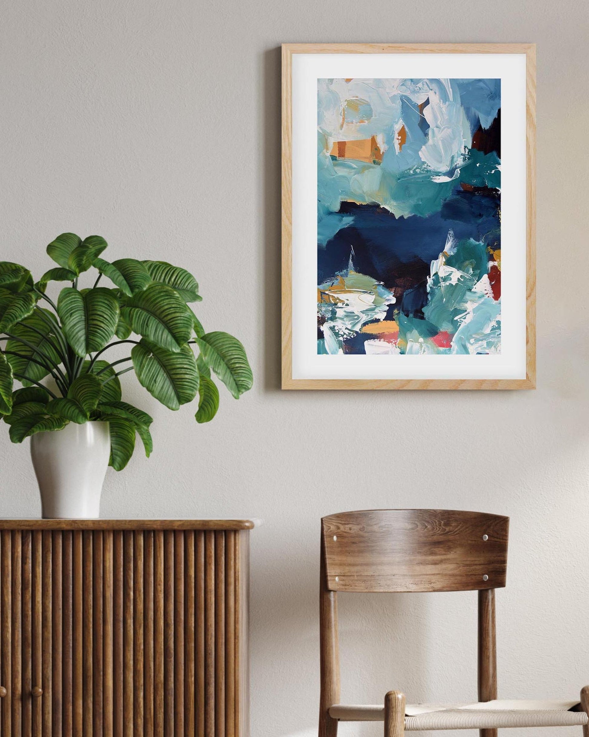 Room interior with a plant on a wooden cabinet, abstract art on the wall, and a chair.