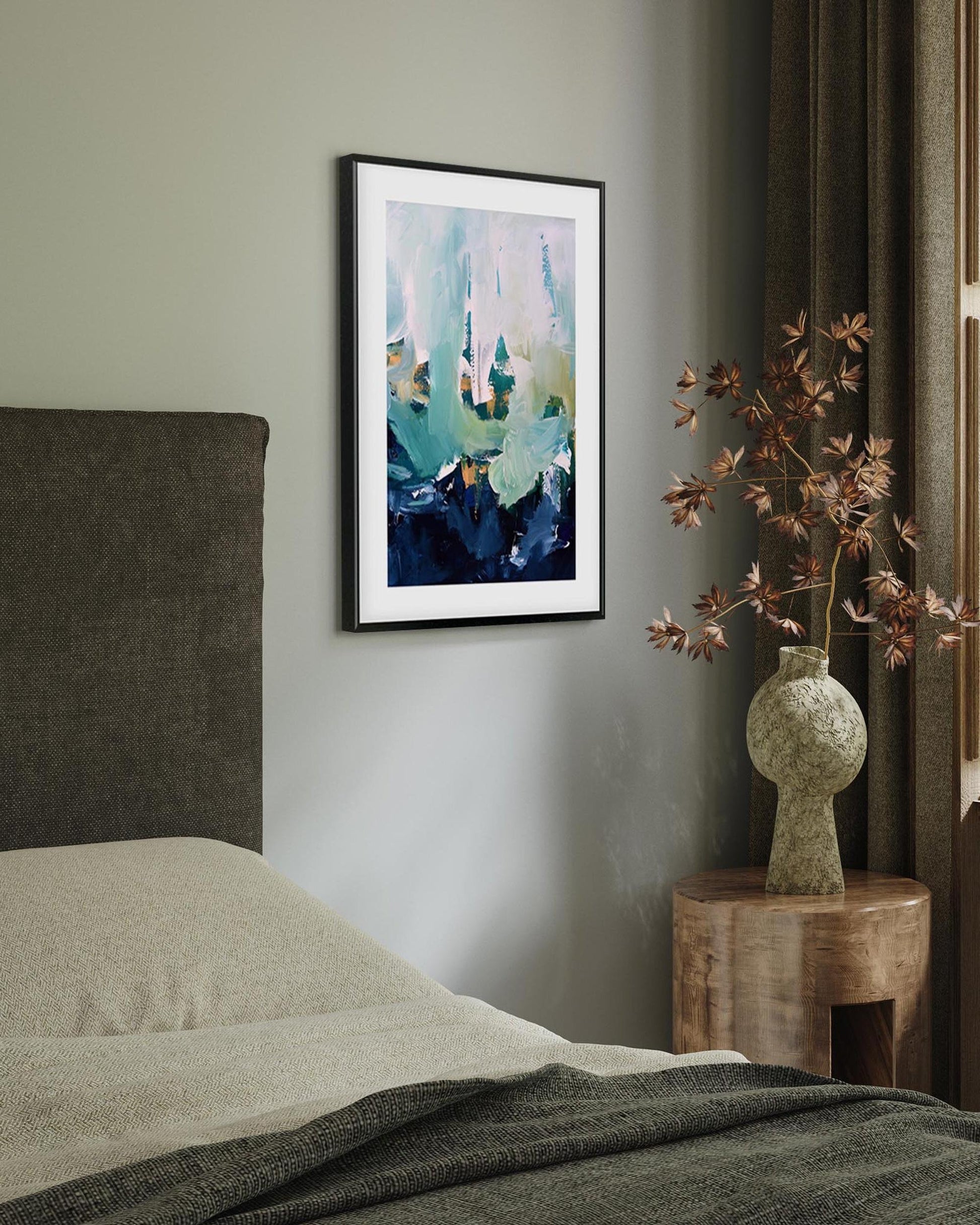 Framed abstract art on a wall above a bed with a vase of flowers on a nightstand.