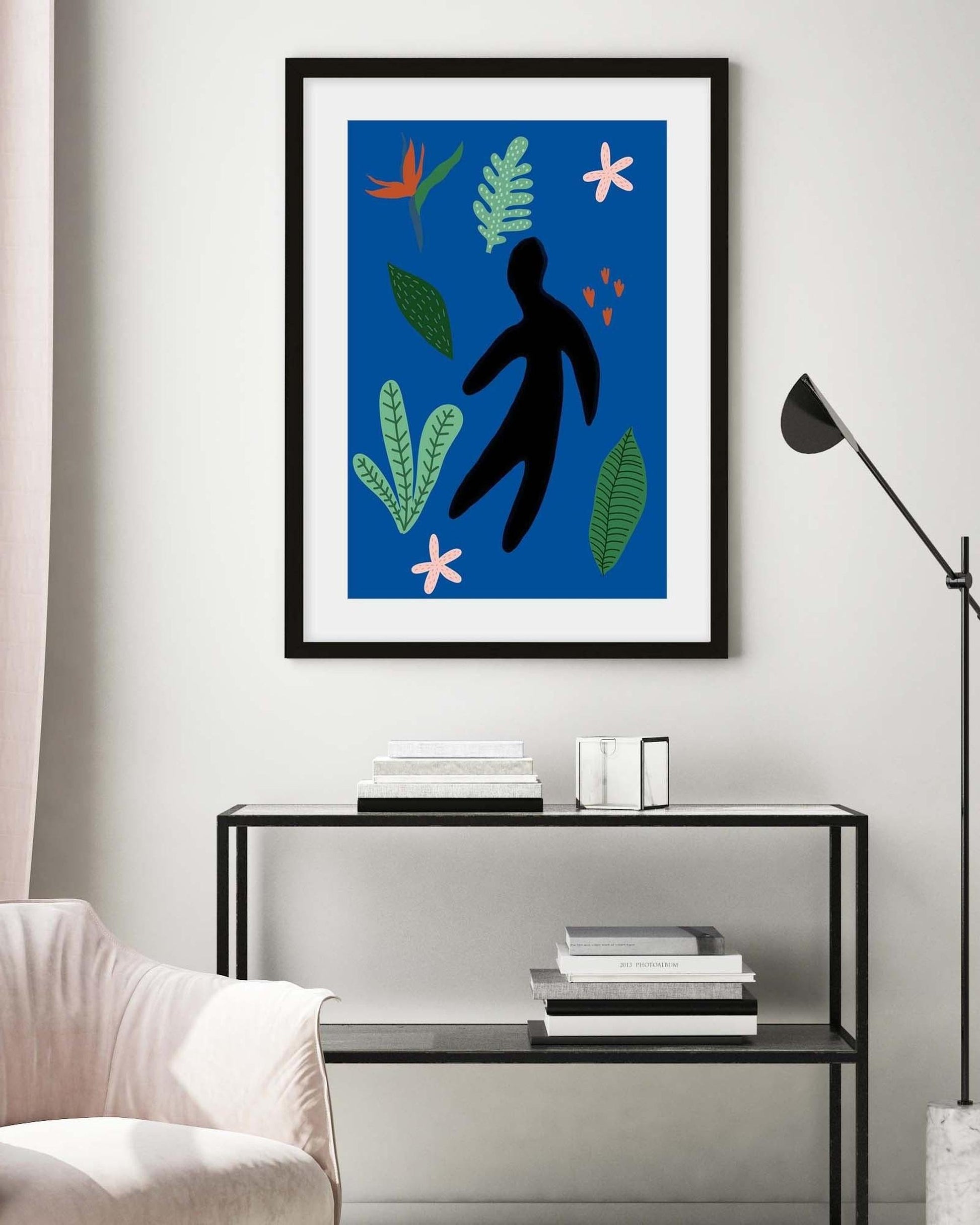 Framed artwork with a black silhouette and colorful leaves on a blue background, displayed in a modern living room.