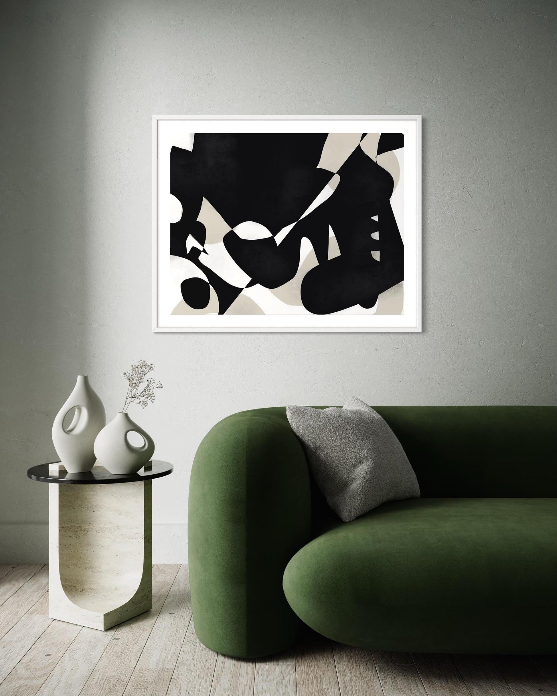 Abstract black and white art print on a wall above a green sofa and side table with decorative items.