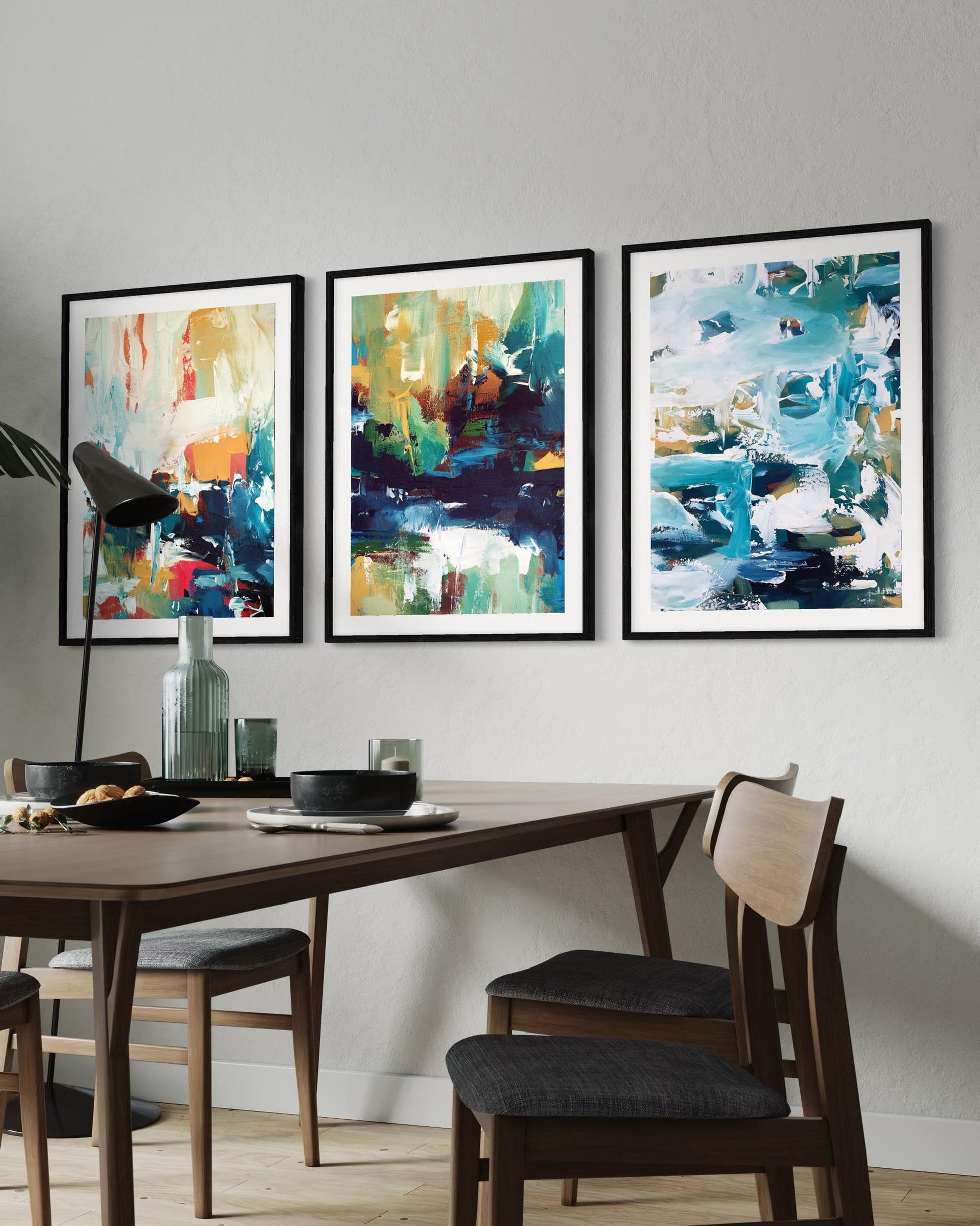 Three abstract paintings on a wall above a dining table with chairs.