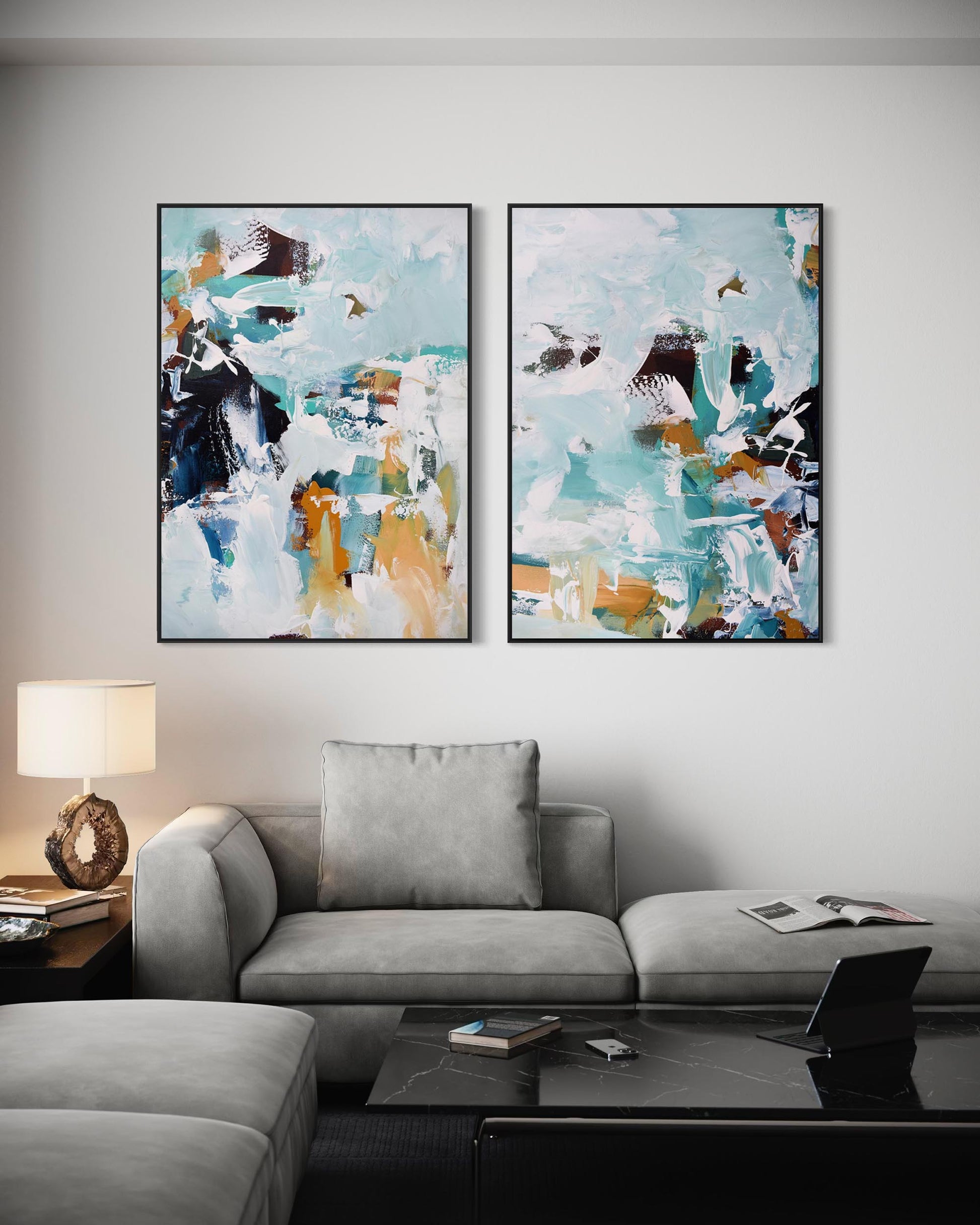 Two abstract paintings on a wall above a gray sofa in a living room.
