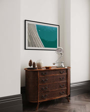 Wooden dresser with decorative items against a white wall with a framed picture of a dock.
