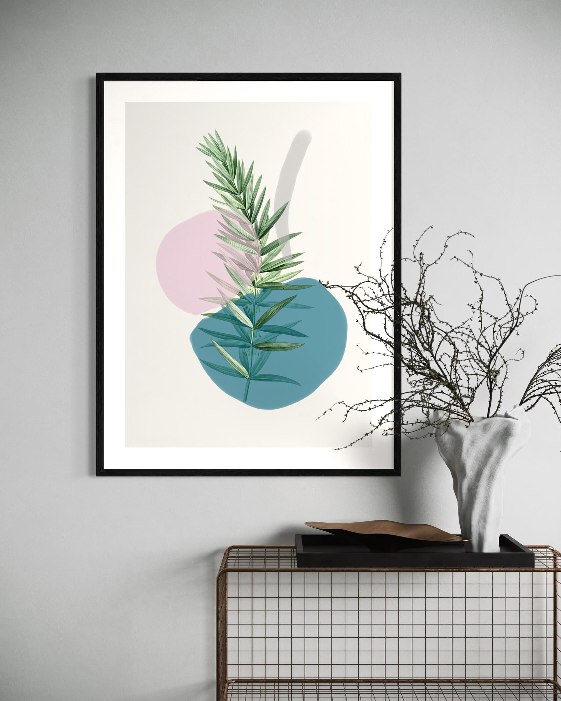 Framed artwork with green leaves and colorful circles on a wall above a black metal shelf.