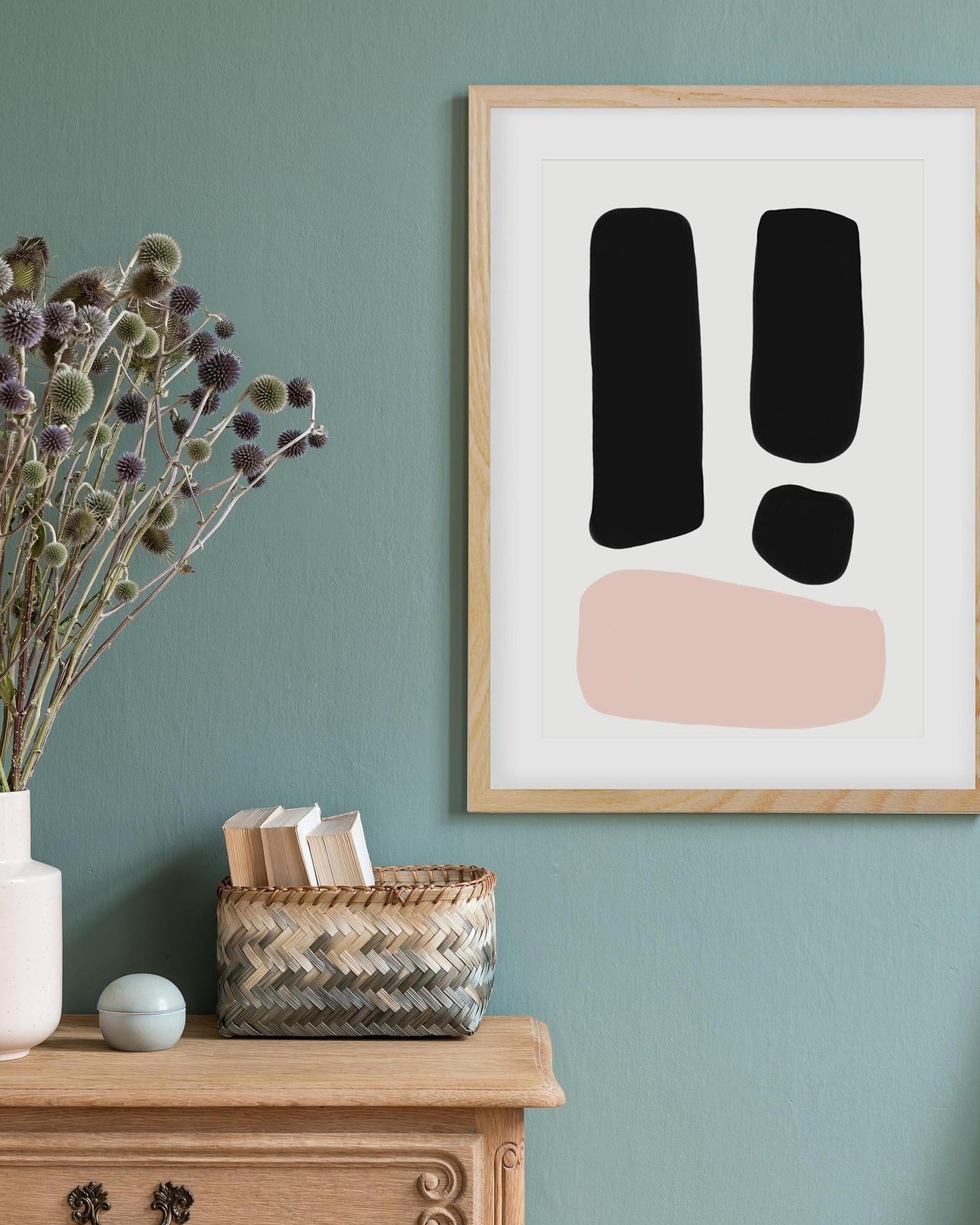 Framed abstract art with exclamation marks on a teal wall above a wooden cabinet.