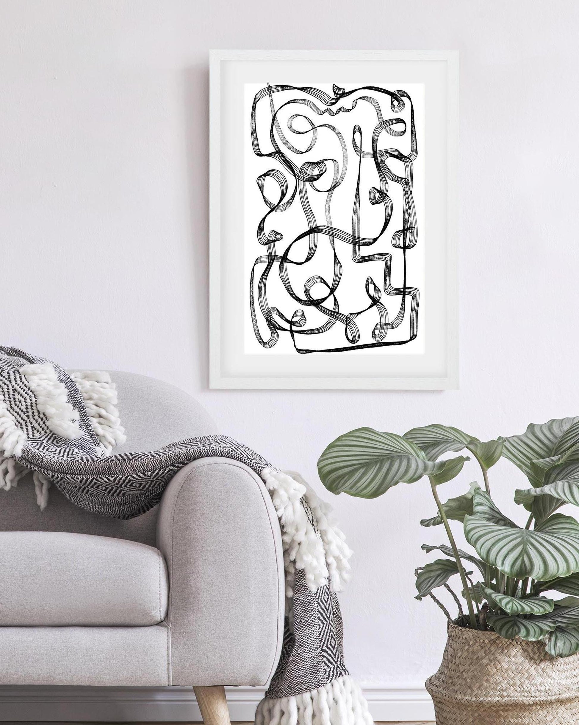 Abstract black and white artwork on a wall above a sofa with a plant in the foreground.