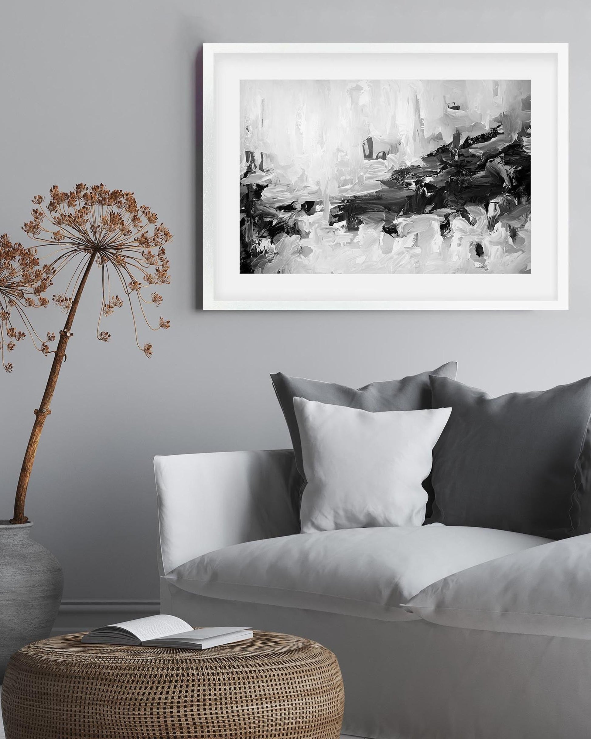 Framed abstract black and white artwork on a gray wall above a sofa with decorative pillows.