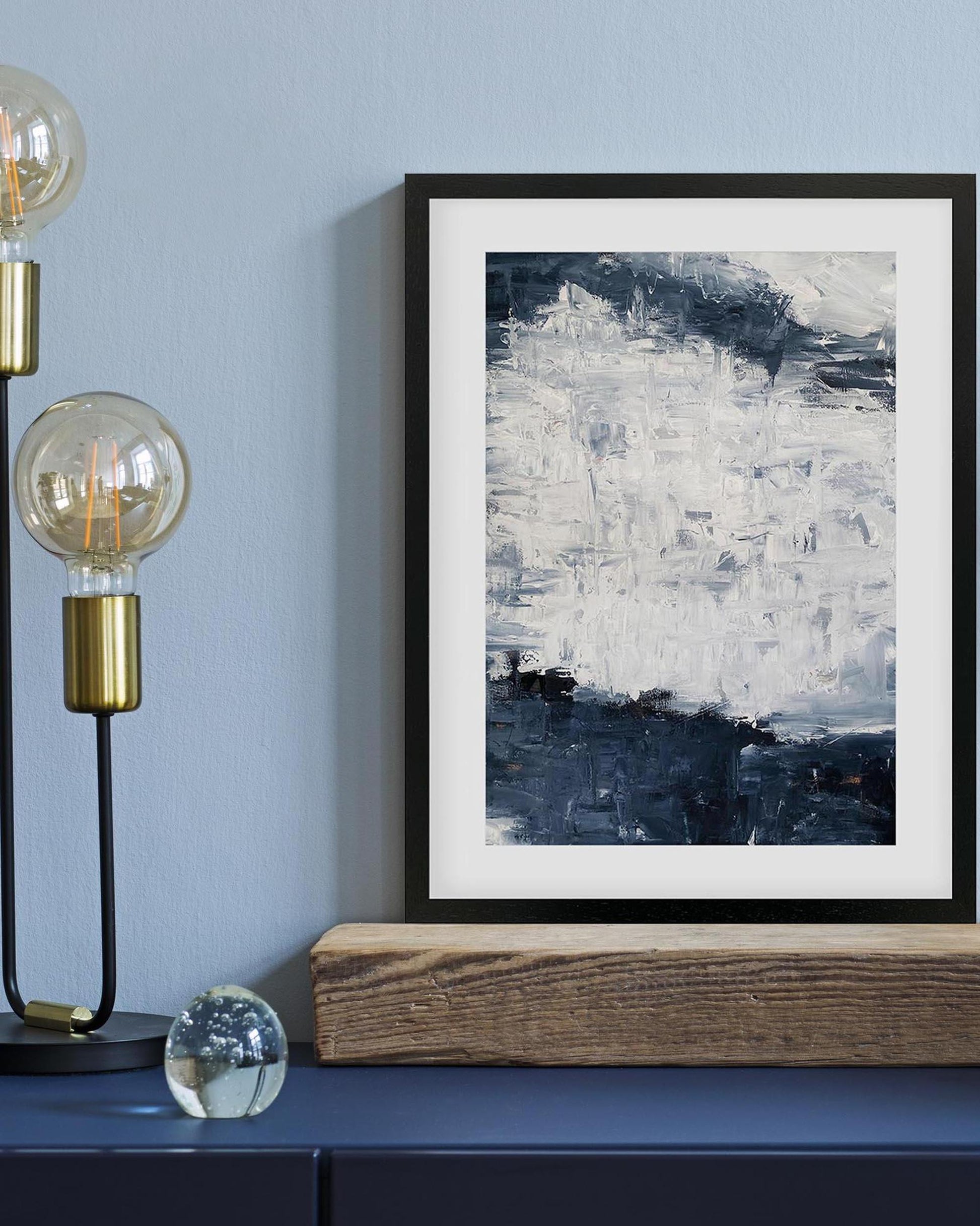 Framed abstract art piece on a wall with a lamp and decorative elements below.