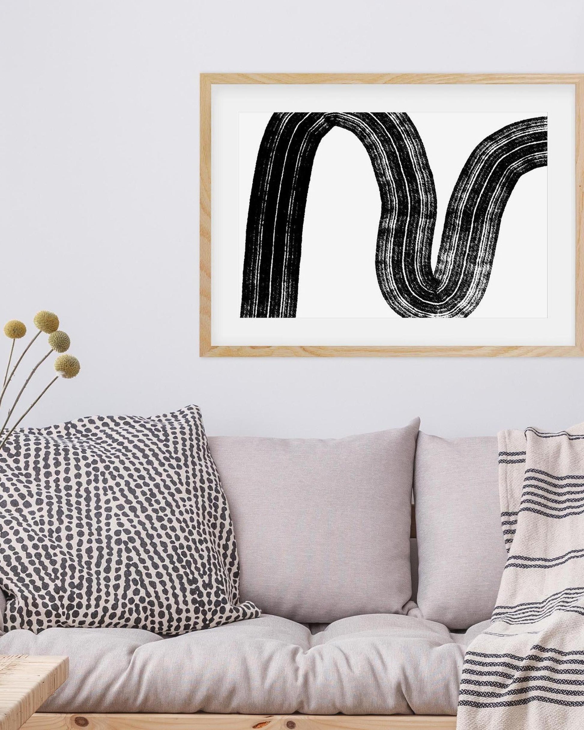 Framed abstract art print above a sofa with decorative pillows and a blanket.