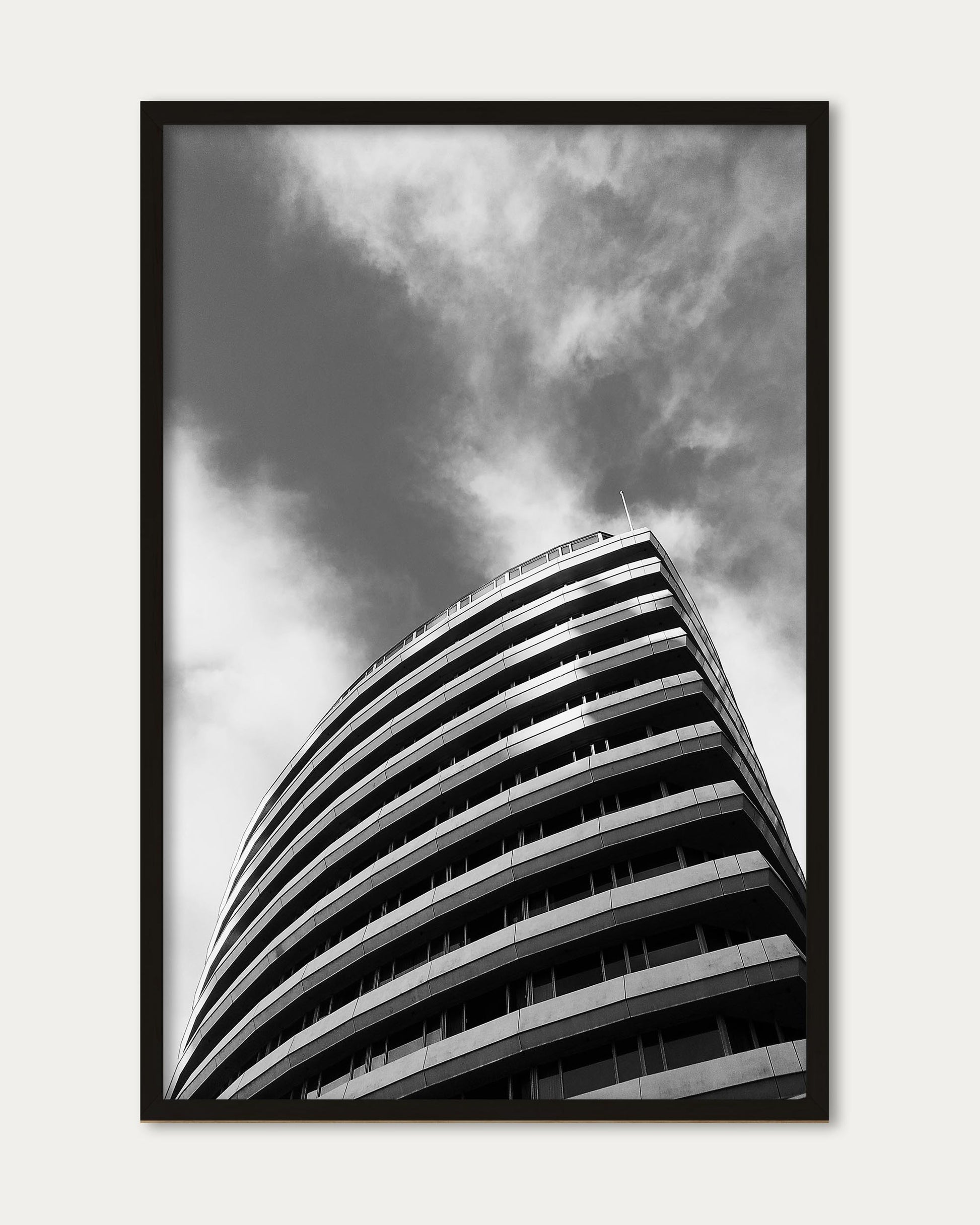 Framed black and white photograph of a curved building against a cloudy sky