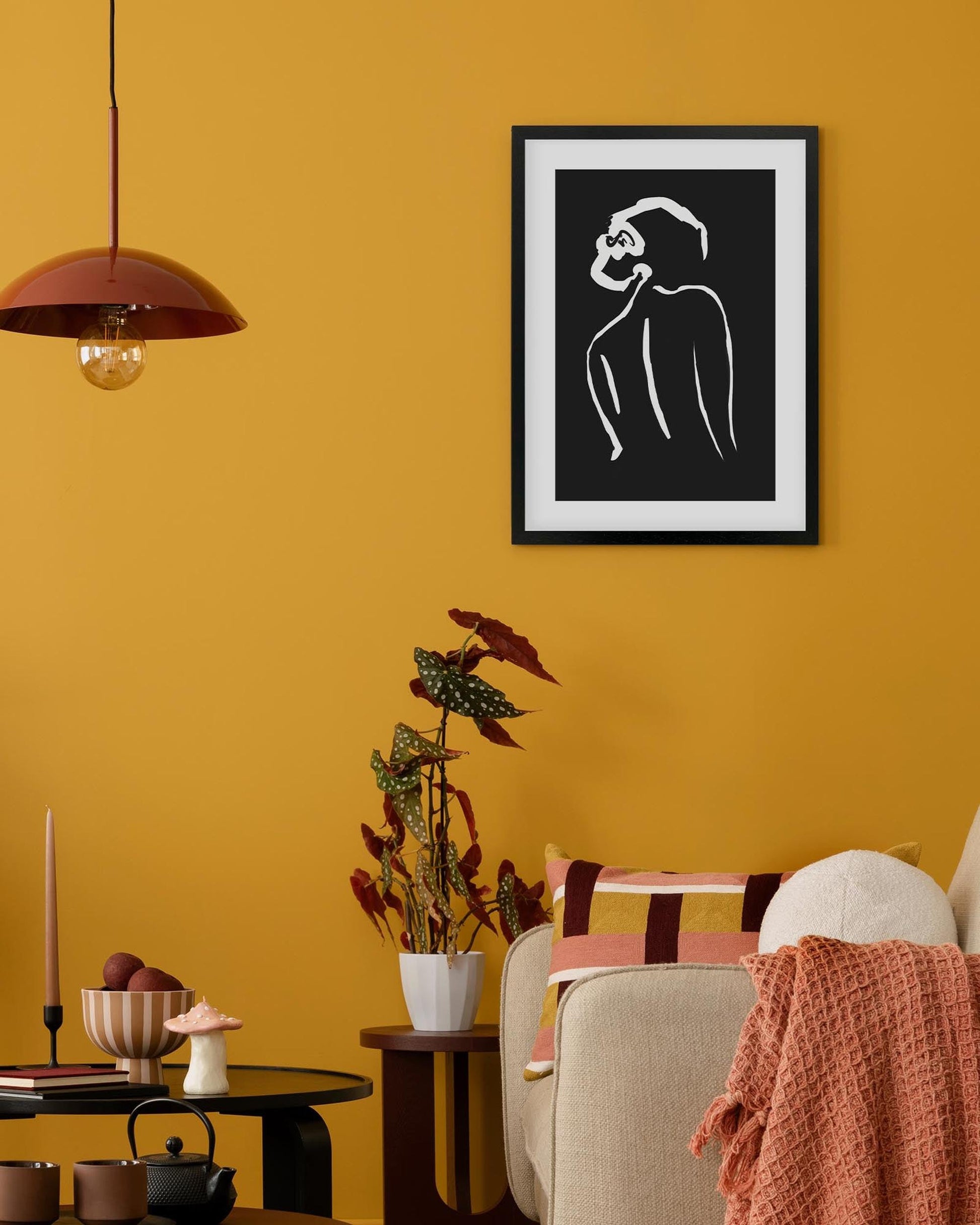 Framed black and white abstract art on a yellow wall with decor elements.