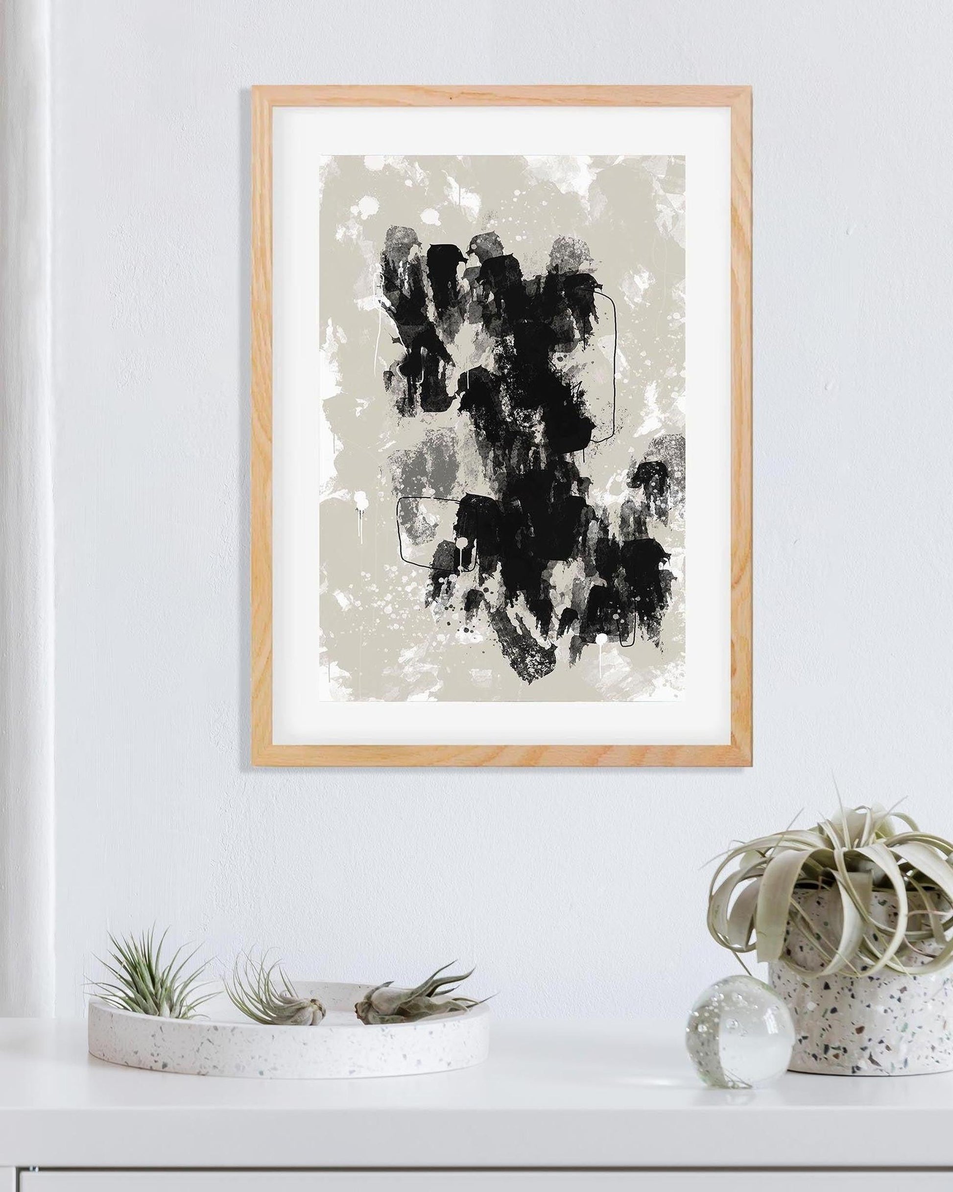 Framed abstract art print on a white wall with decorative plants below.