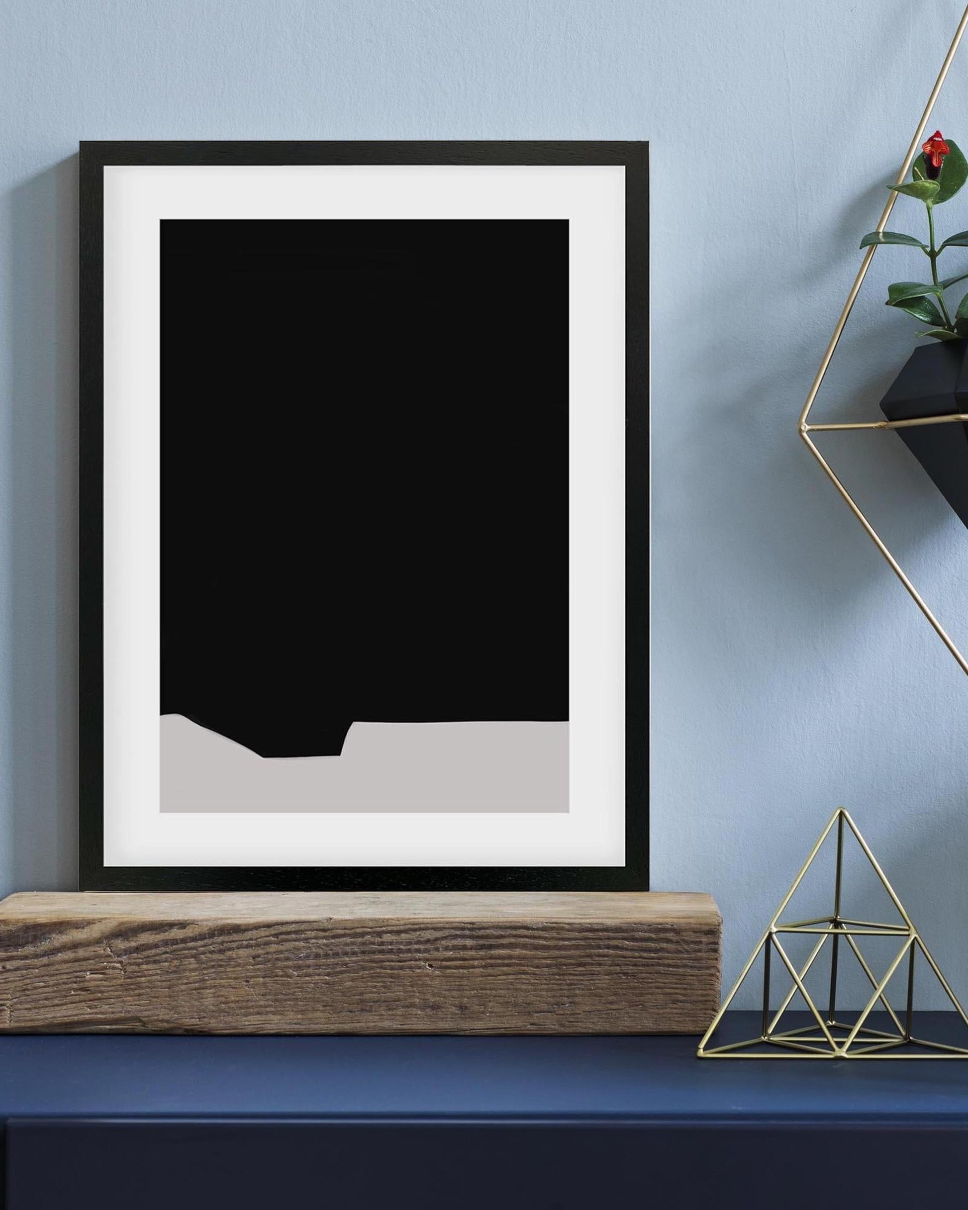 Framed black and white abstract art piece on a blue wall with decorative elements.