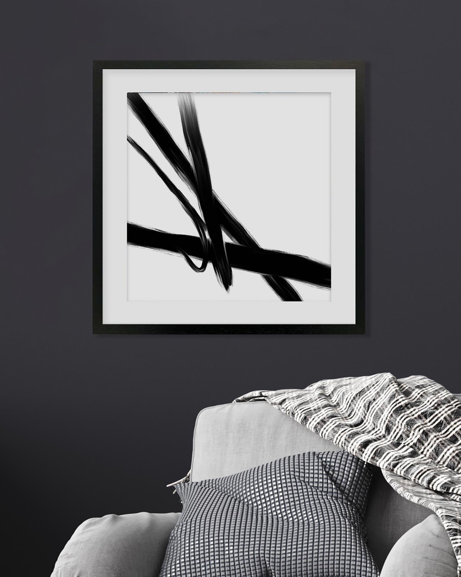 Framed black and white abstract art print on a dark wall above a sofa.