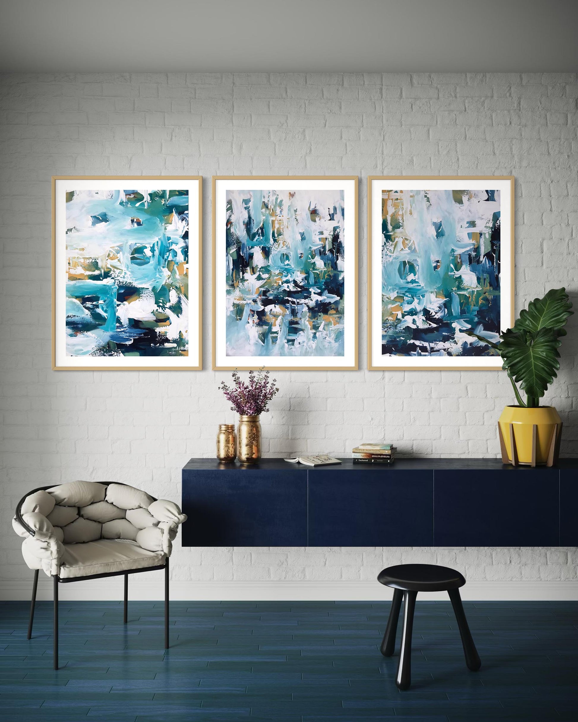 Three abstract art pieces on a wall above a blue console table with decorative items.