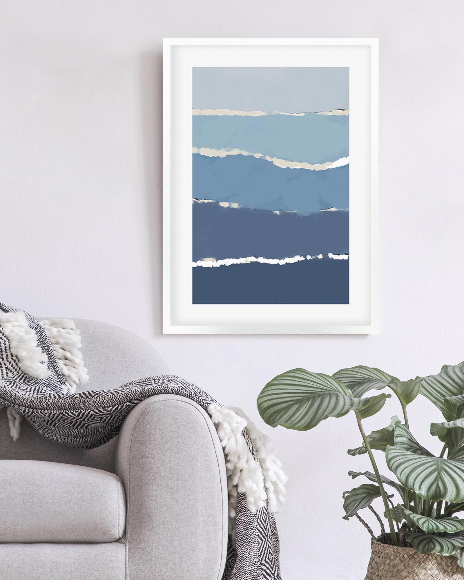 Framed abstract art print with blue and white brushstroke design on a wall above a sofa.