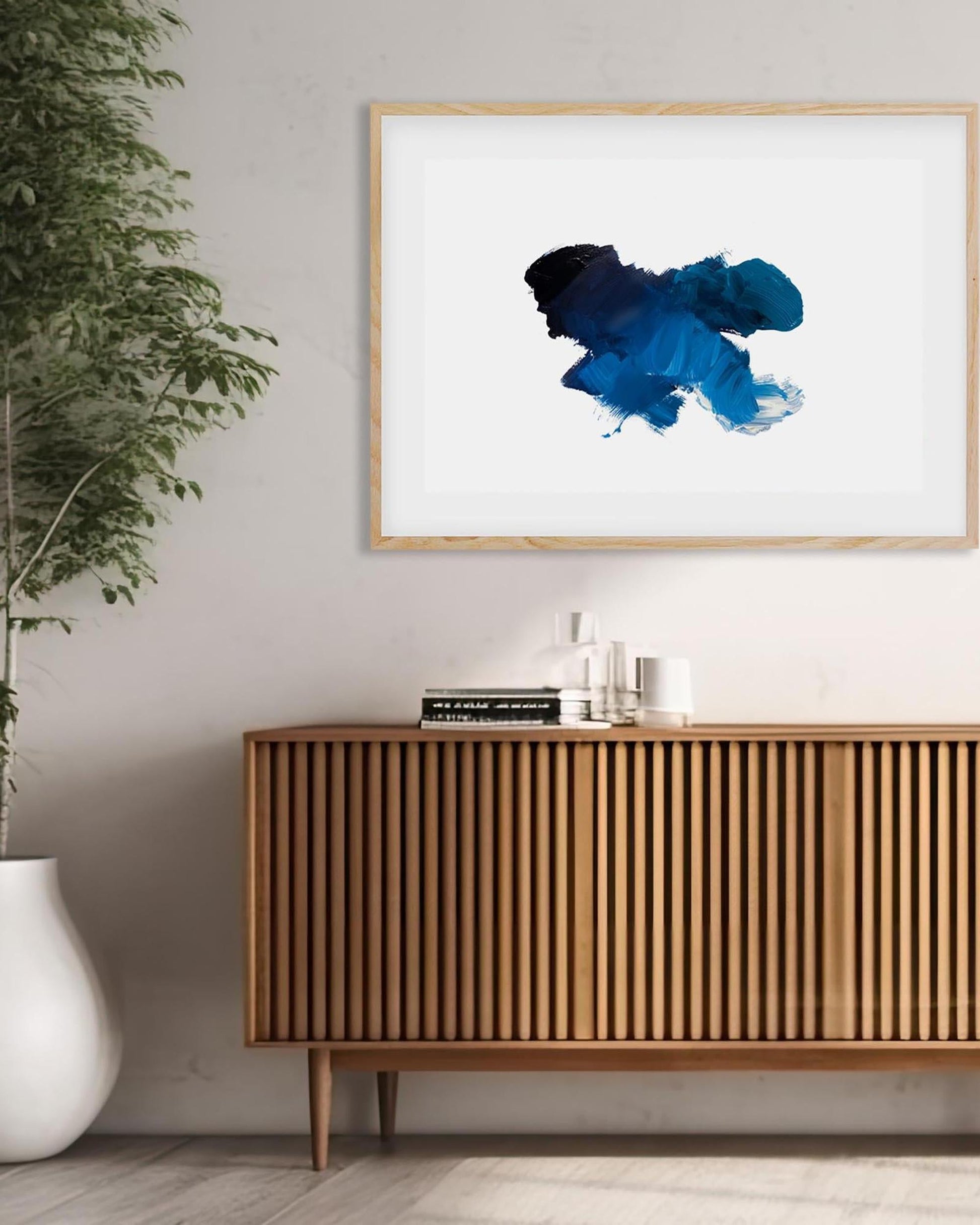 Framed abstract art piece on a wall above a wooden sideboard with decor items.