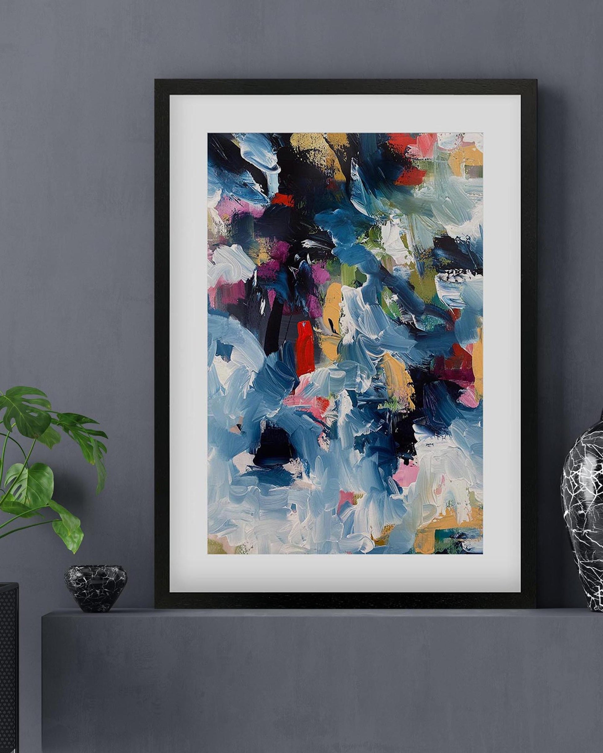 Framed abstract art print on a gray wall with decorative items.