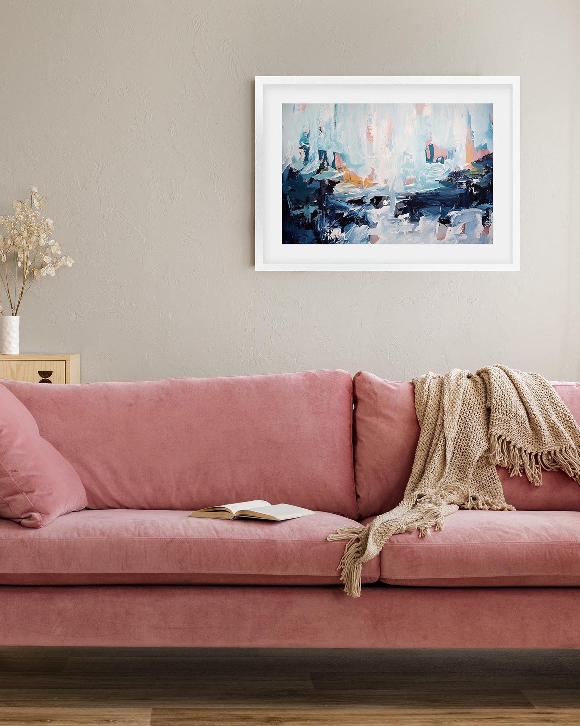 Pink sofa with a blanket and book, framed abstract art on the wall