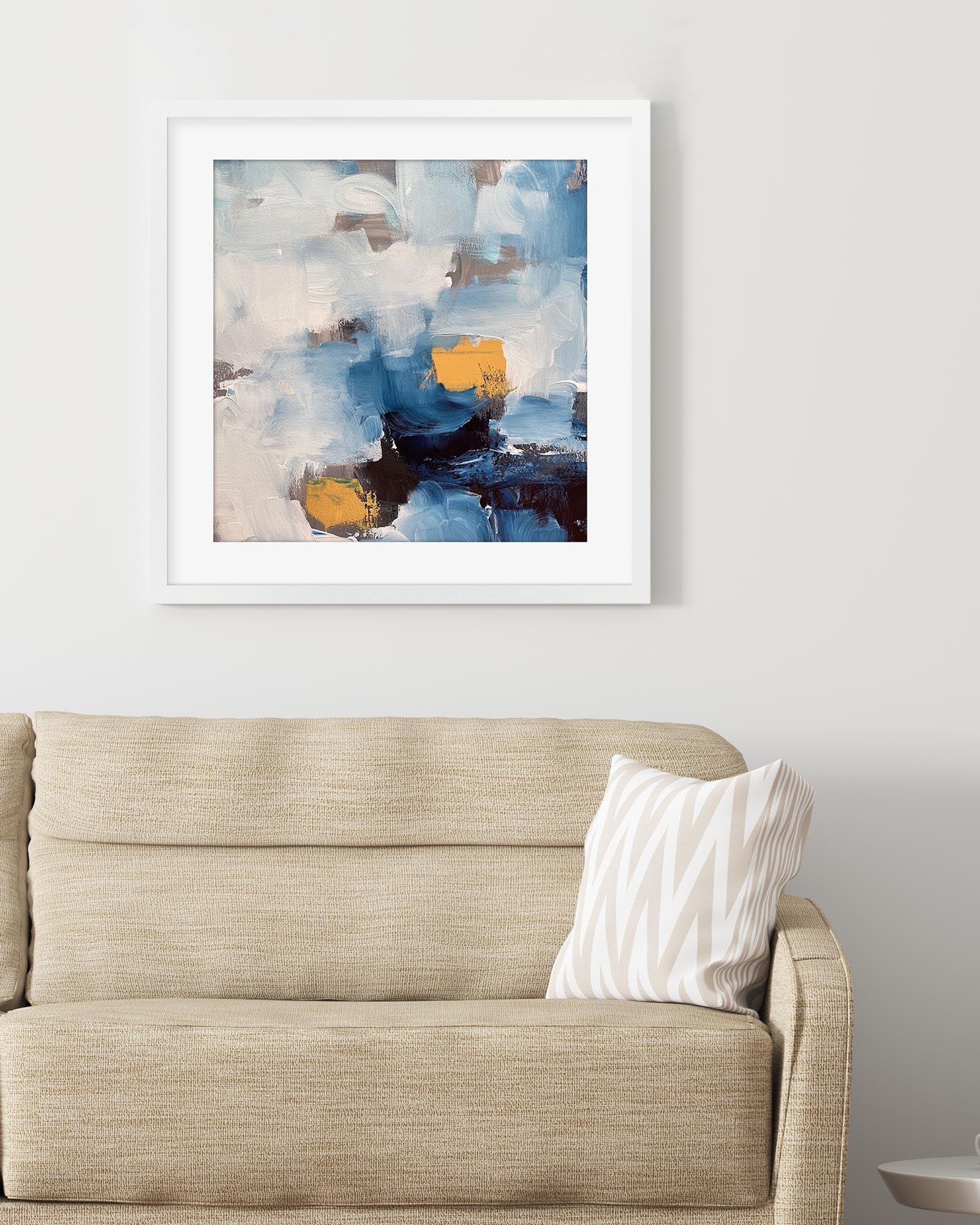Abstract painting with blue, yellow, and white colors on a wall above a beige sofa.