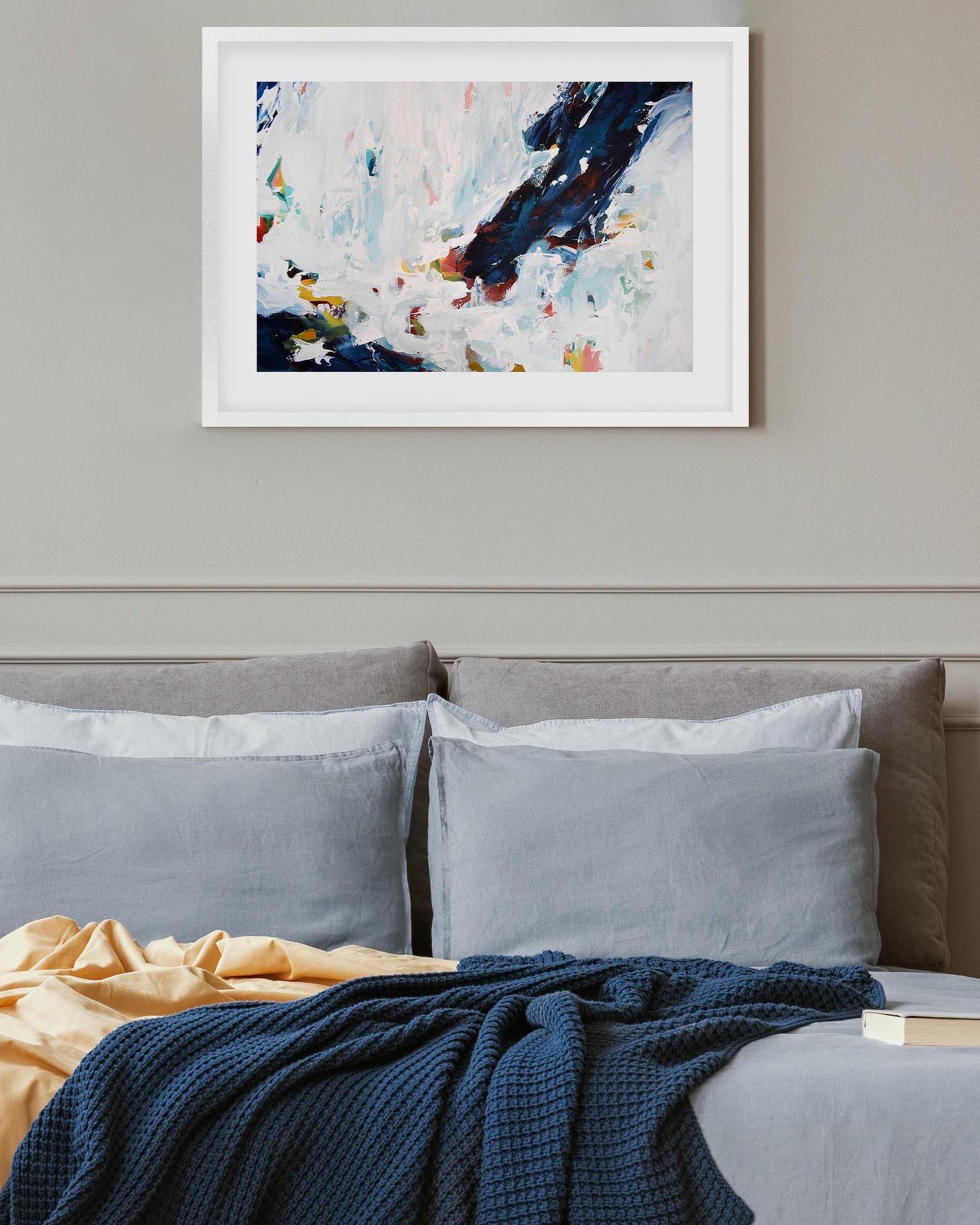 Abstract painting above a bed with gray bedding and a colorful blanket.