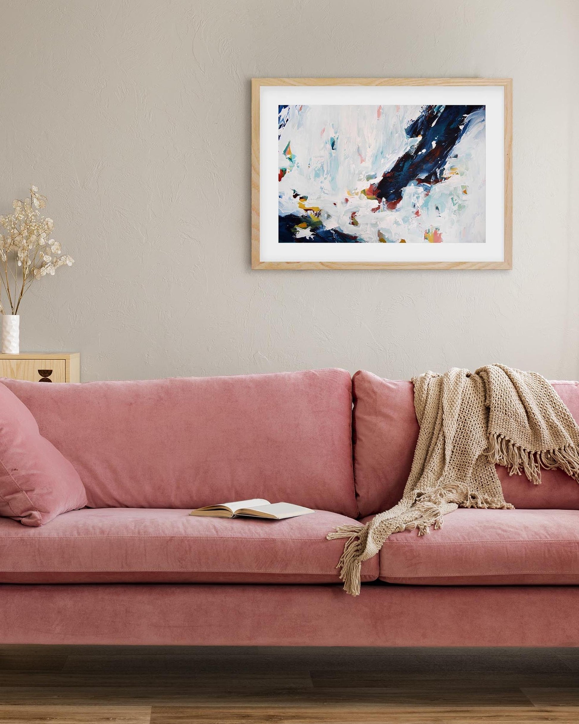 Pink sofa in a living room with a colorful abstract painting on the wall.