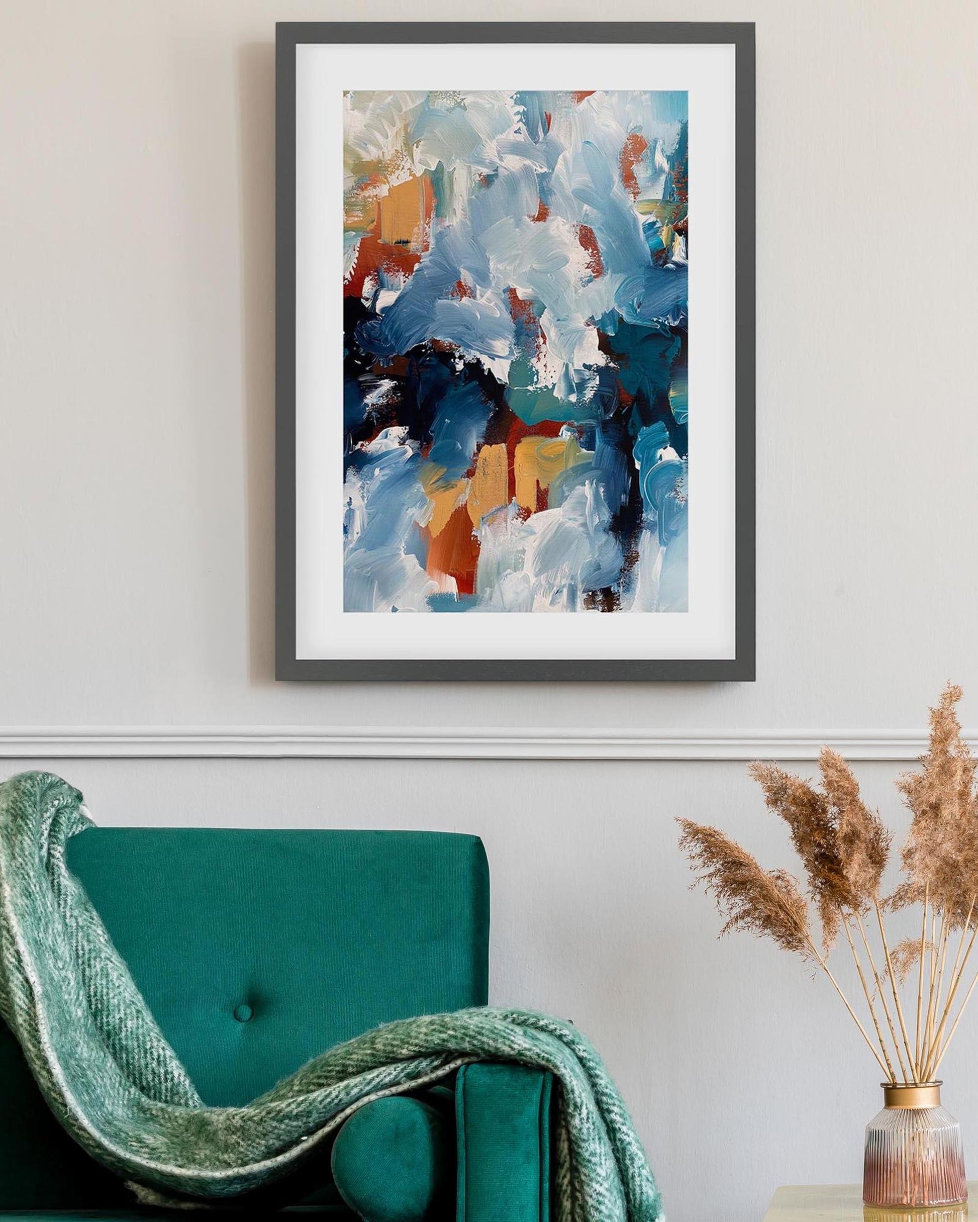 Abstract art print on a wall above a teal chair with a decorative plant.