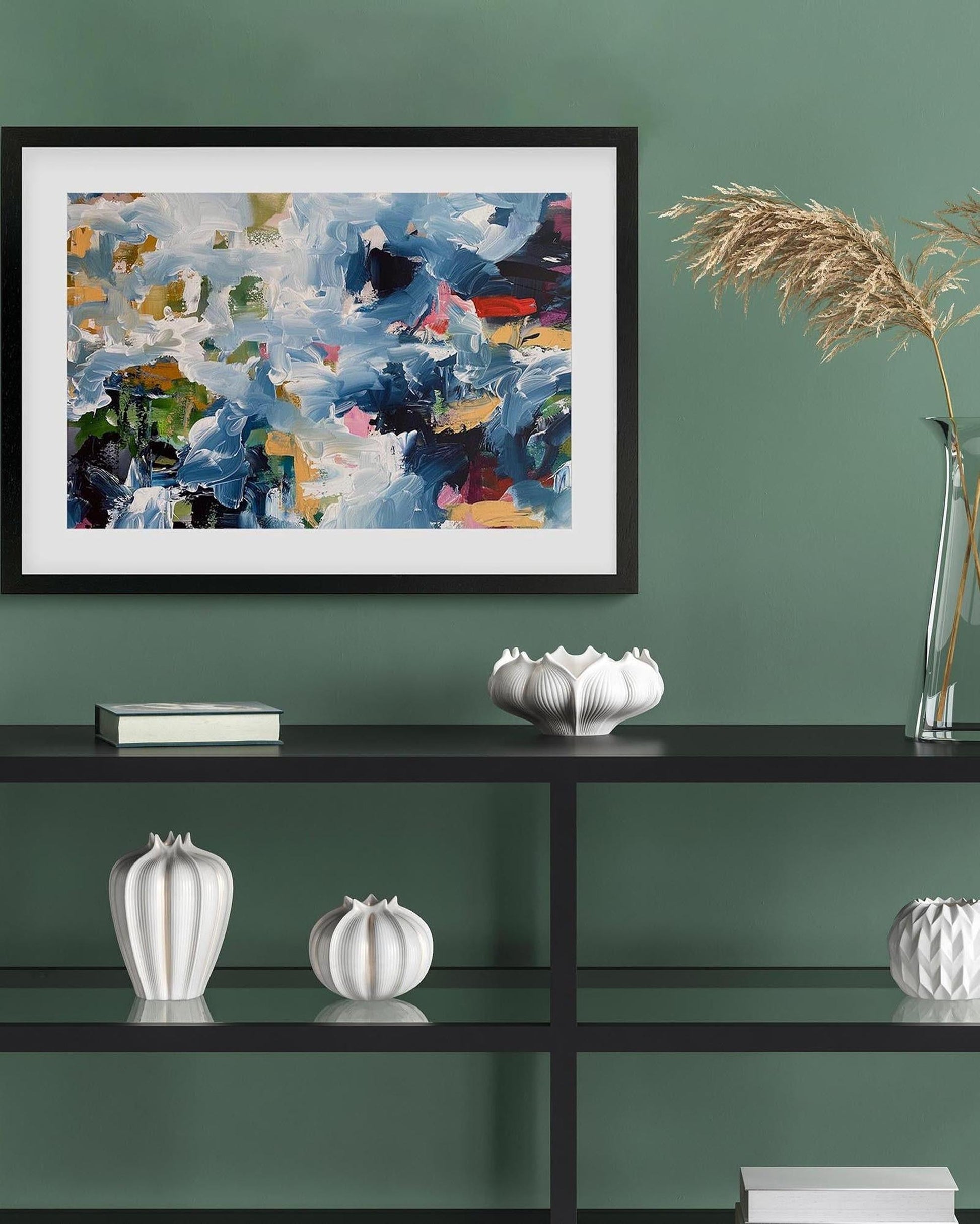 Framed abstract painting on a green wall with decorative items on a shelf.
