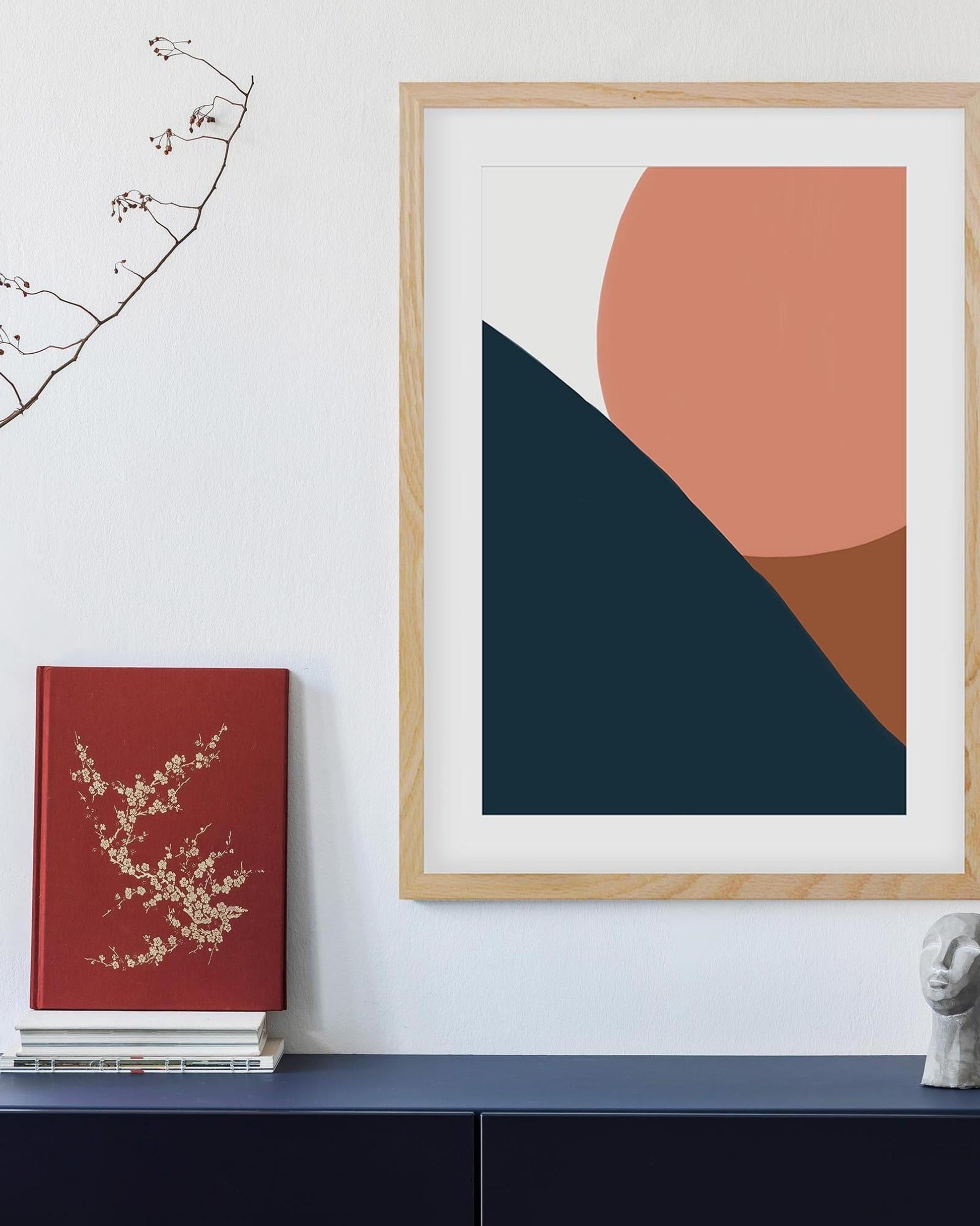 Framed abstract art with geometric shapes on a wall next to a red book.