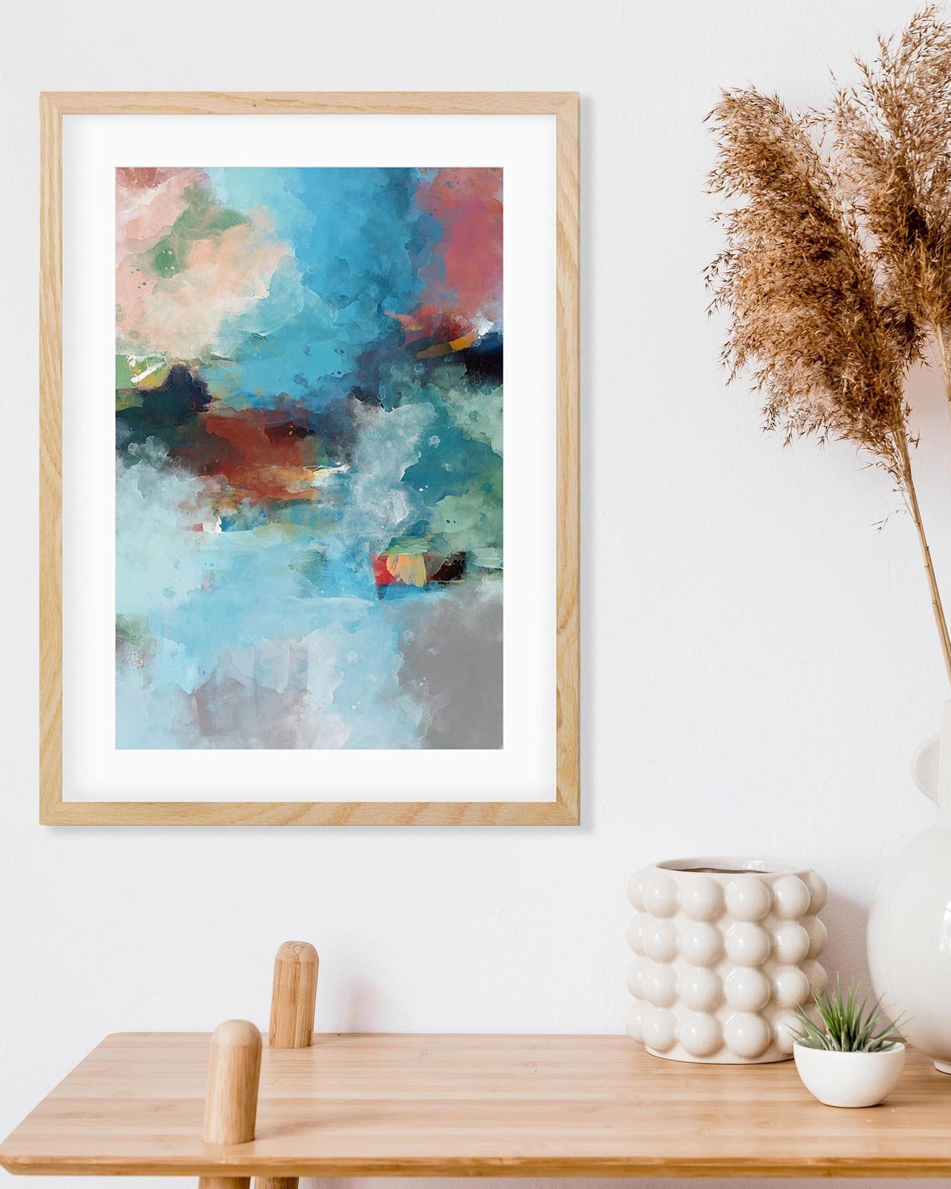 Framed abstract art print on a wall above a wooden table with decorative items.