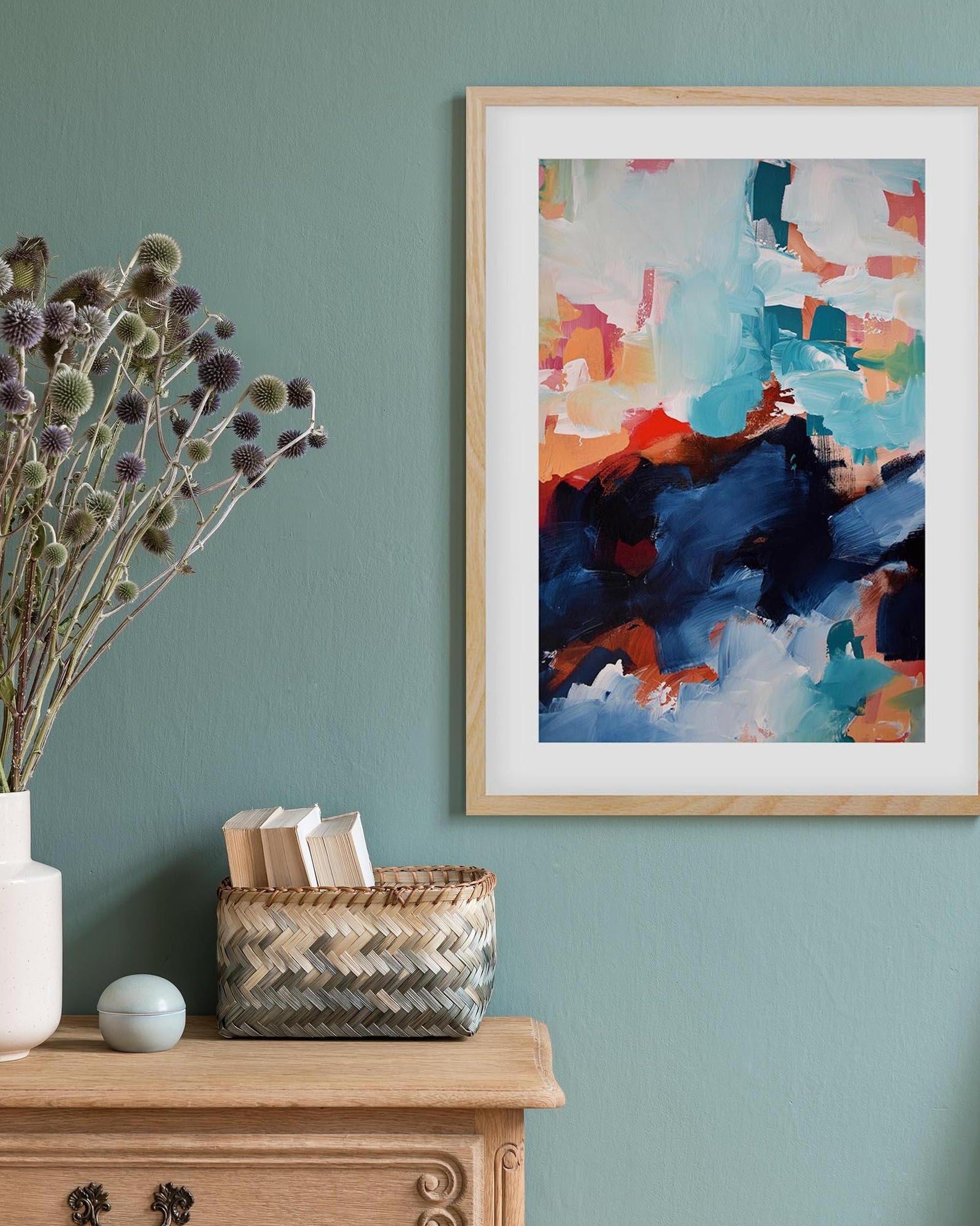 Colorful abstract painting on a teal wall with a wooden cabinet and decorative items.