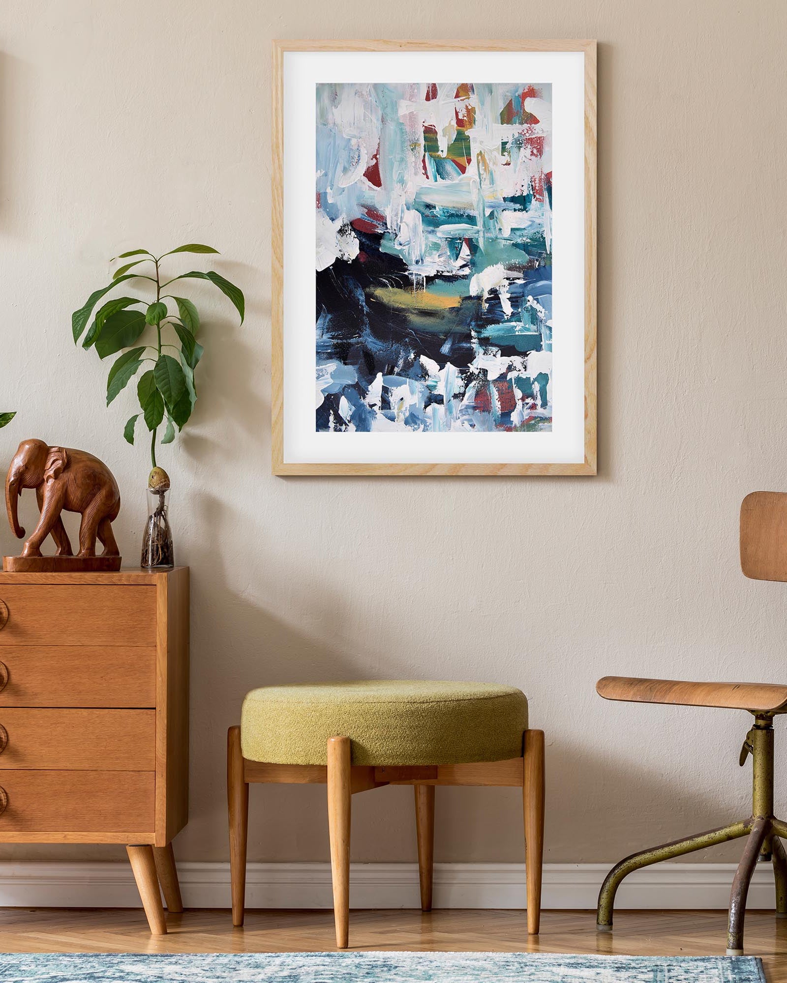 Framed abstract art on a wall above a wooden cabinet with decorative items.