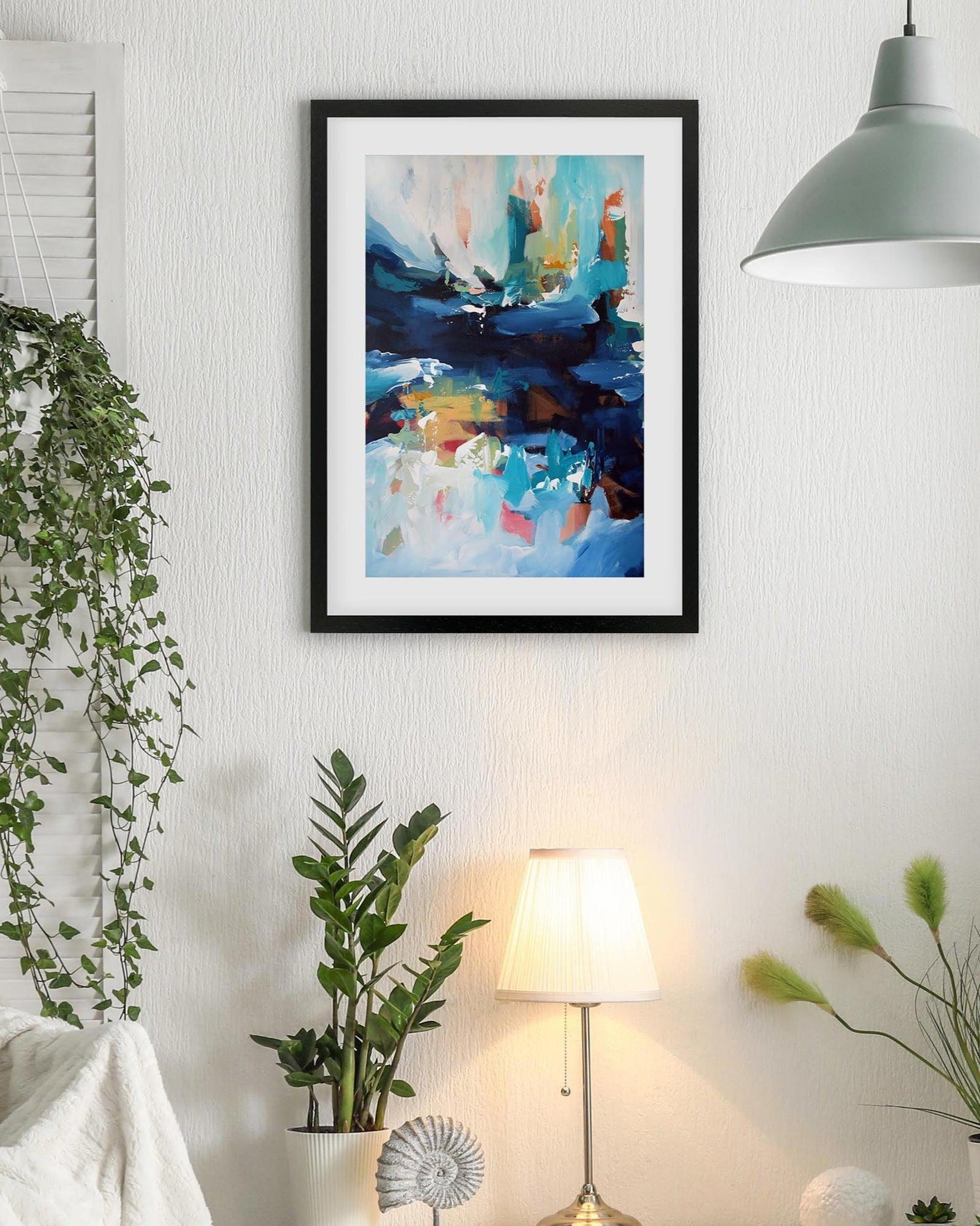 Living room with a framed abstract painting, plants, and a lamp.