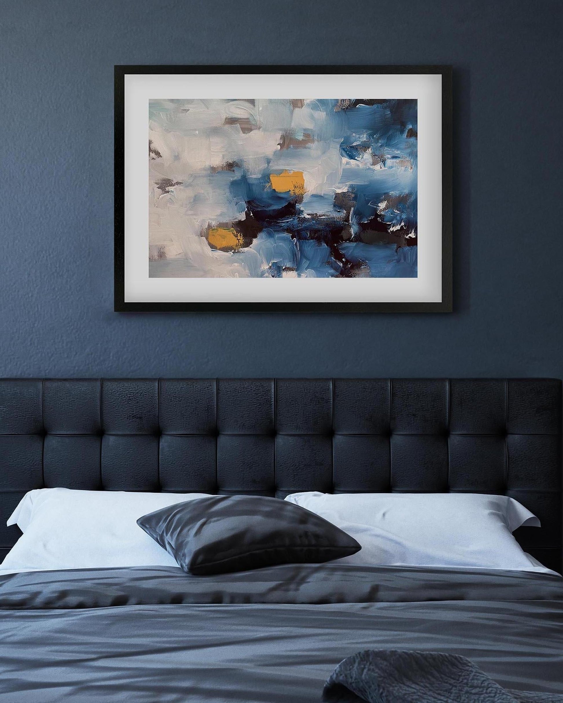Abstract painting on a wall above a bed with a tufted headboard.