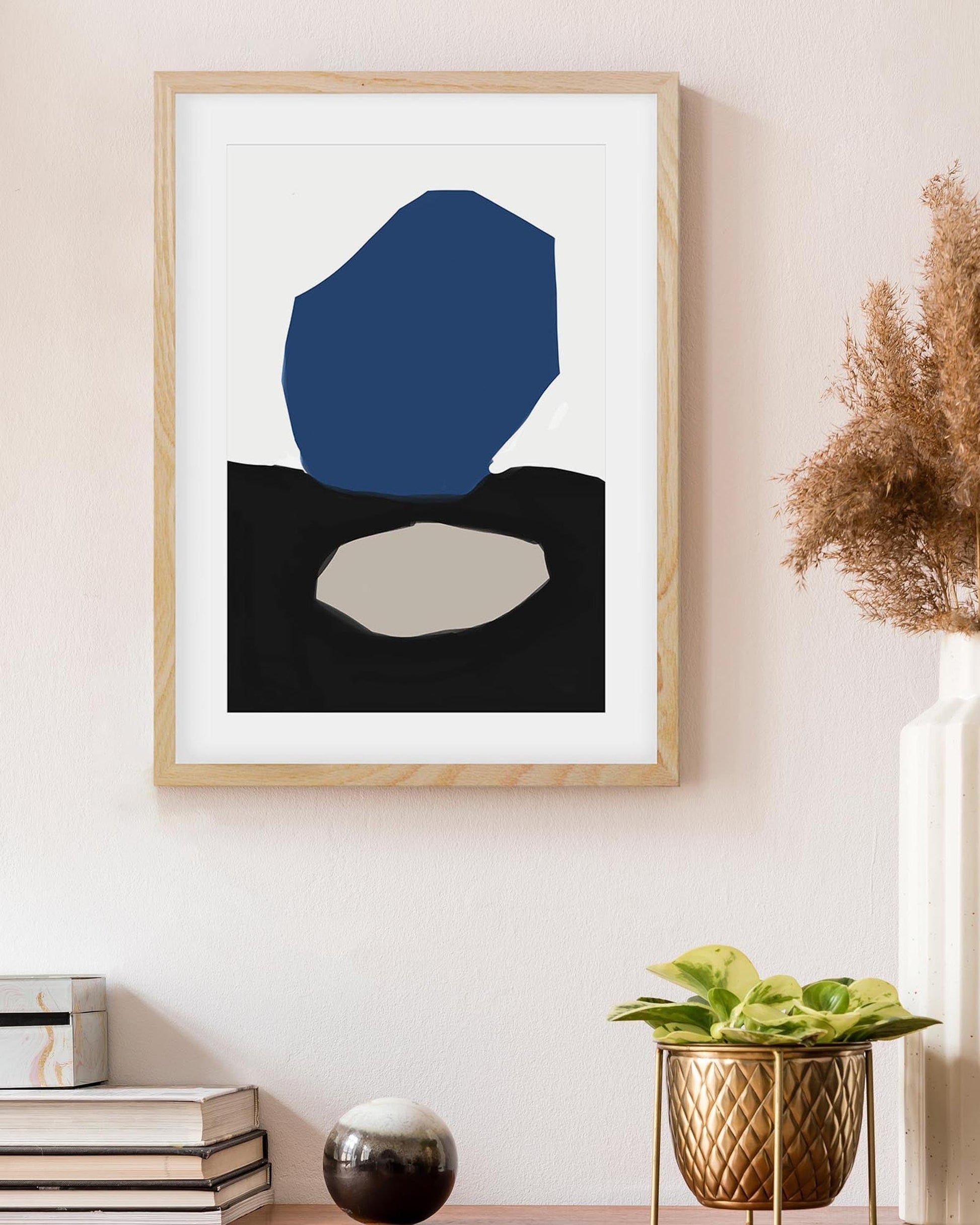 Framed abstract art print with blue and black shapes on a wall, next to decorative items.