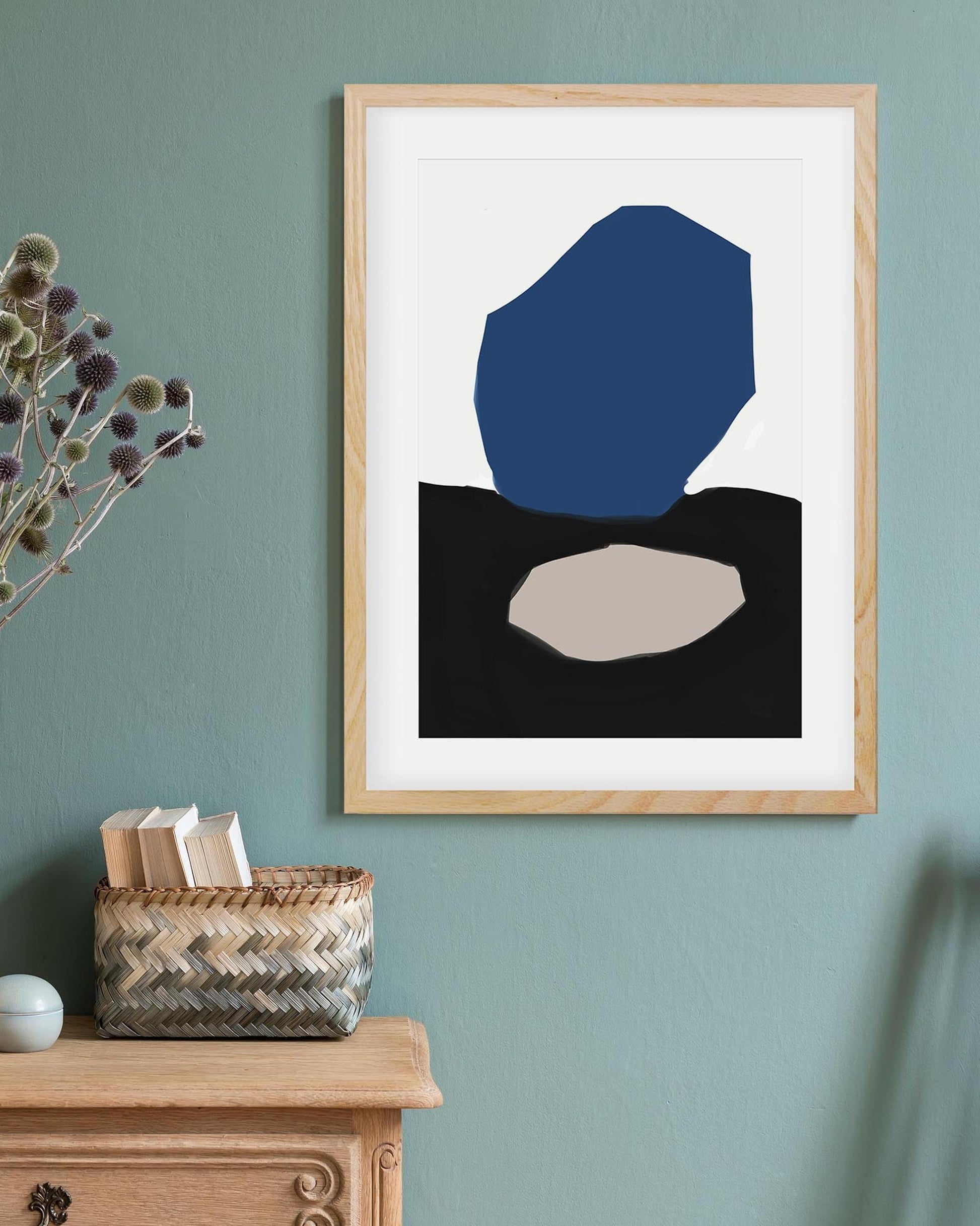 Framed abstract art piece on a wall with a wooden cabinet and basket below.