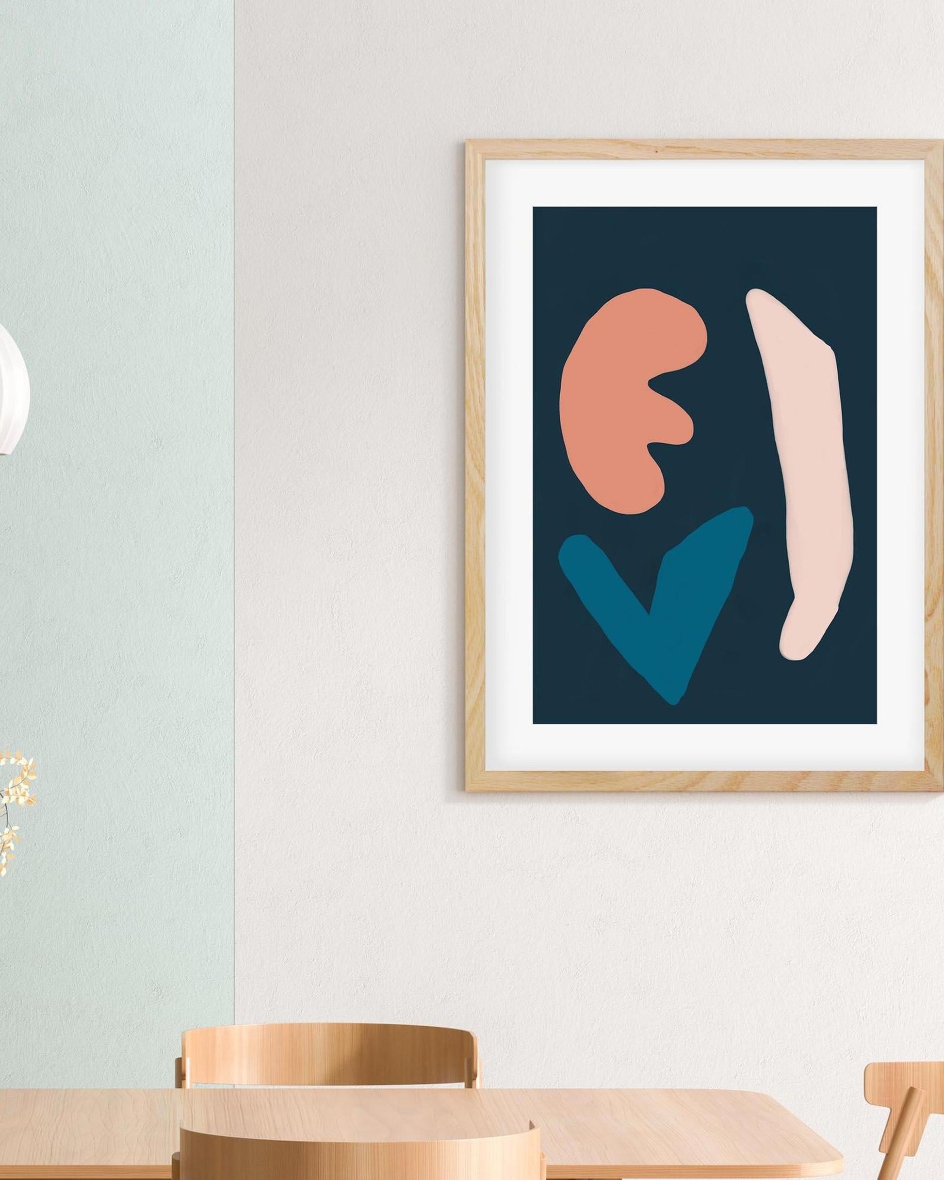 Framed abstract art print with colorful shapes on a wall above a wooden table.