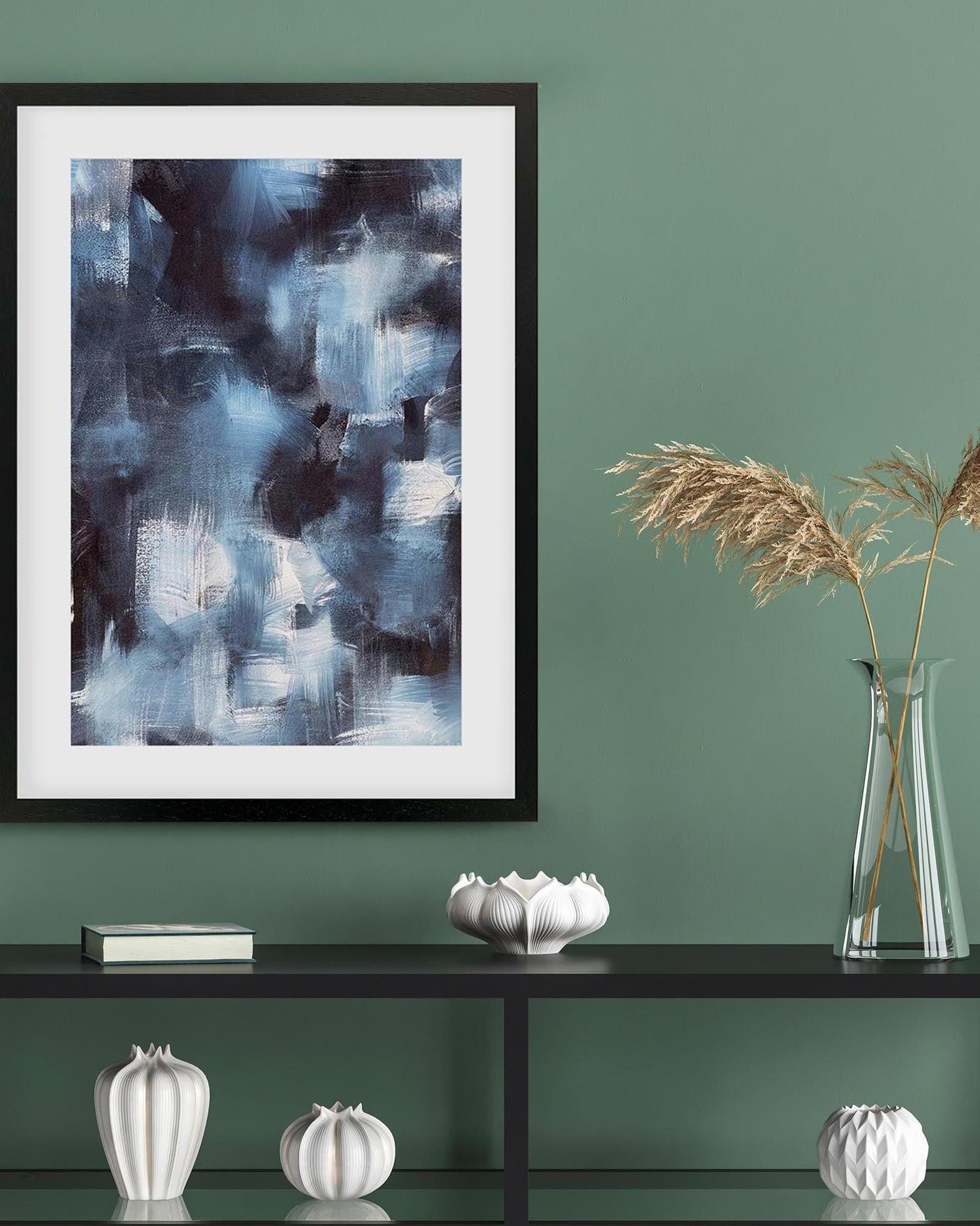 Framed abstract painting on a green wall with decorative items on a shelf.
