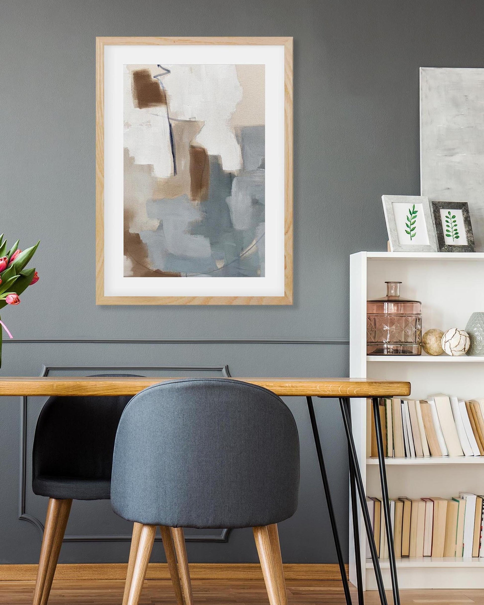 Modern interior with a wooden desk, gray chairs, and abstract art on a gray wall.