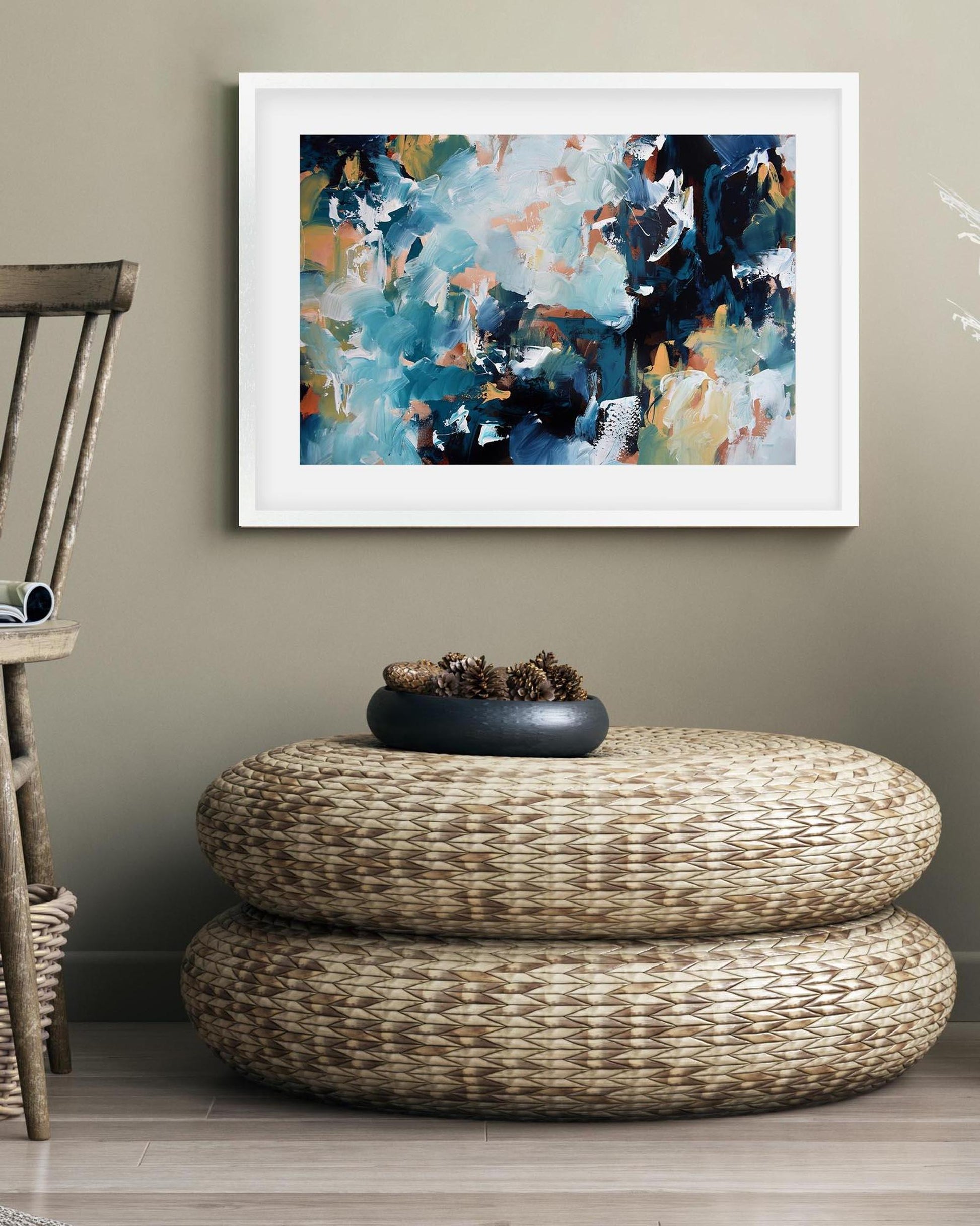 Abstract painting on a wall above a woven ottoman with a decorative bowl.